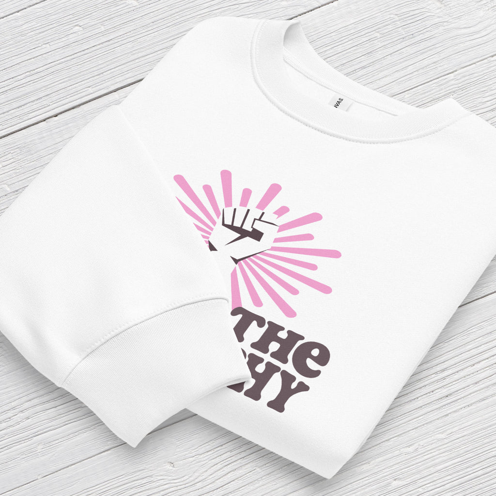 Folded white sweatshirt with a raised fist graphic and pink rays behind it, featuring the text “Smash the Patriarchy.” Shows cuff detail.