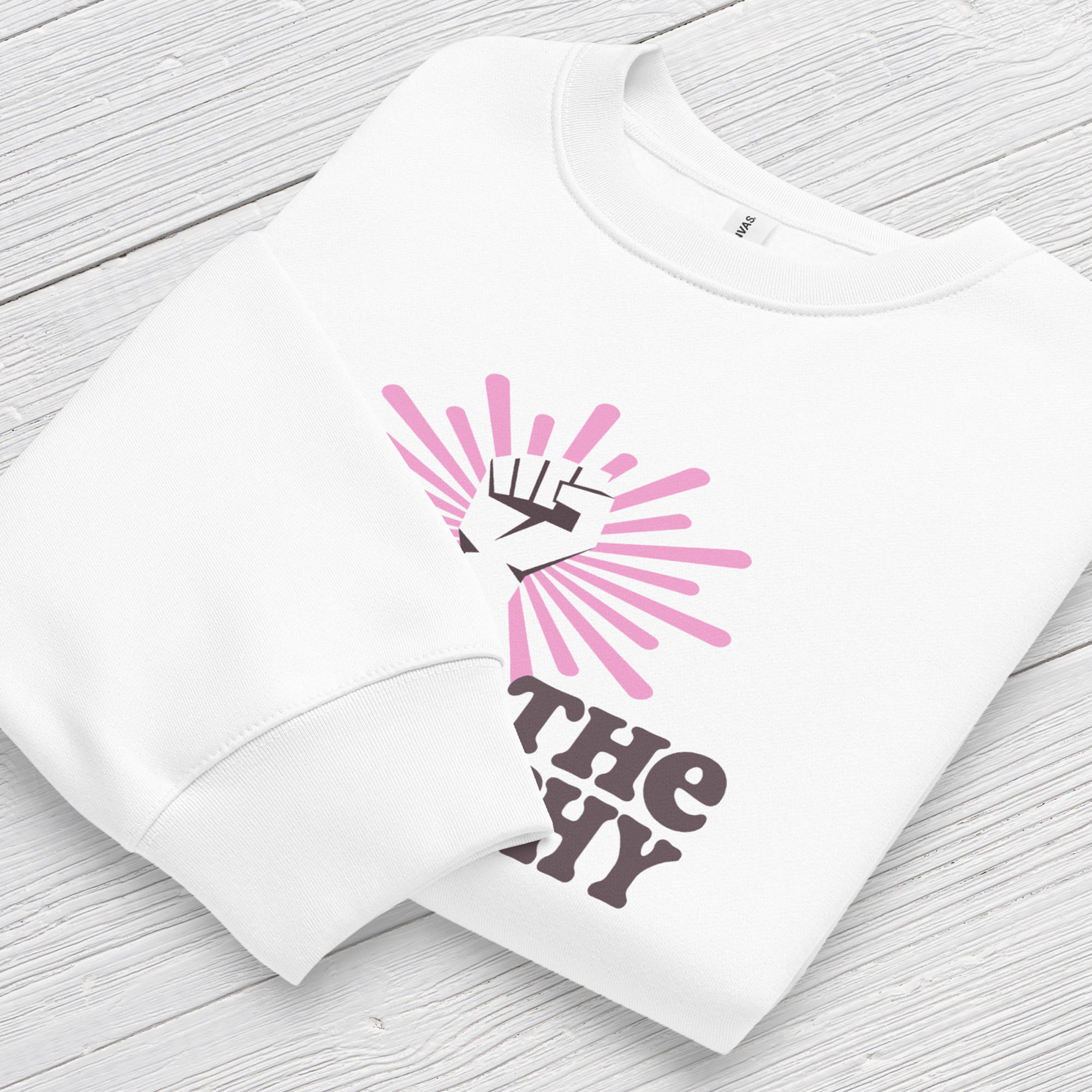 Folded white sweatshirt with a raised fist graphic and pink rays behind it, featuring the text “Smash the Patriarchy.” Shows cuff detail.