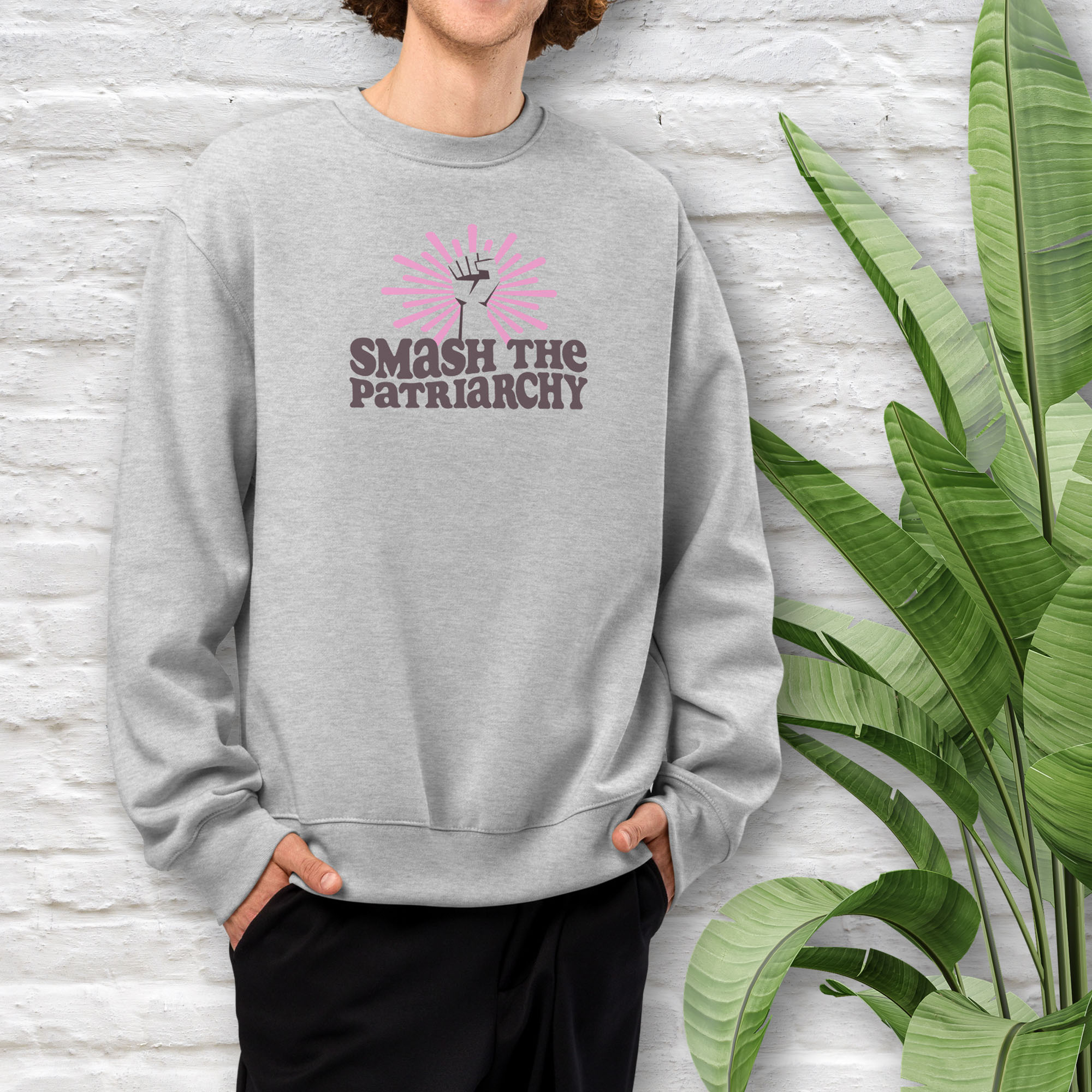 Male model wearing grey sweatshirt with a raised fist graphic and pink rays behind it, featuring the text “Smash the Patriarchy.”