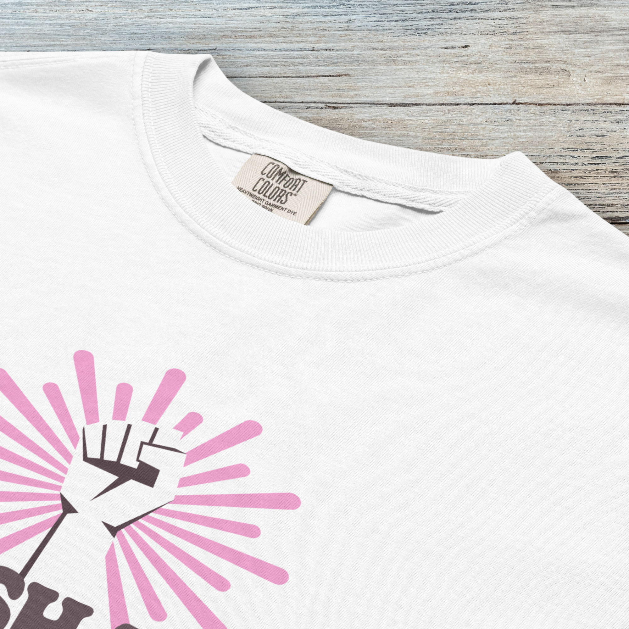 Closeup detail of white t-shirt with a raised fist graphic and pink rays behind it, featuring the text “Smash the Patriarchy.”