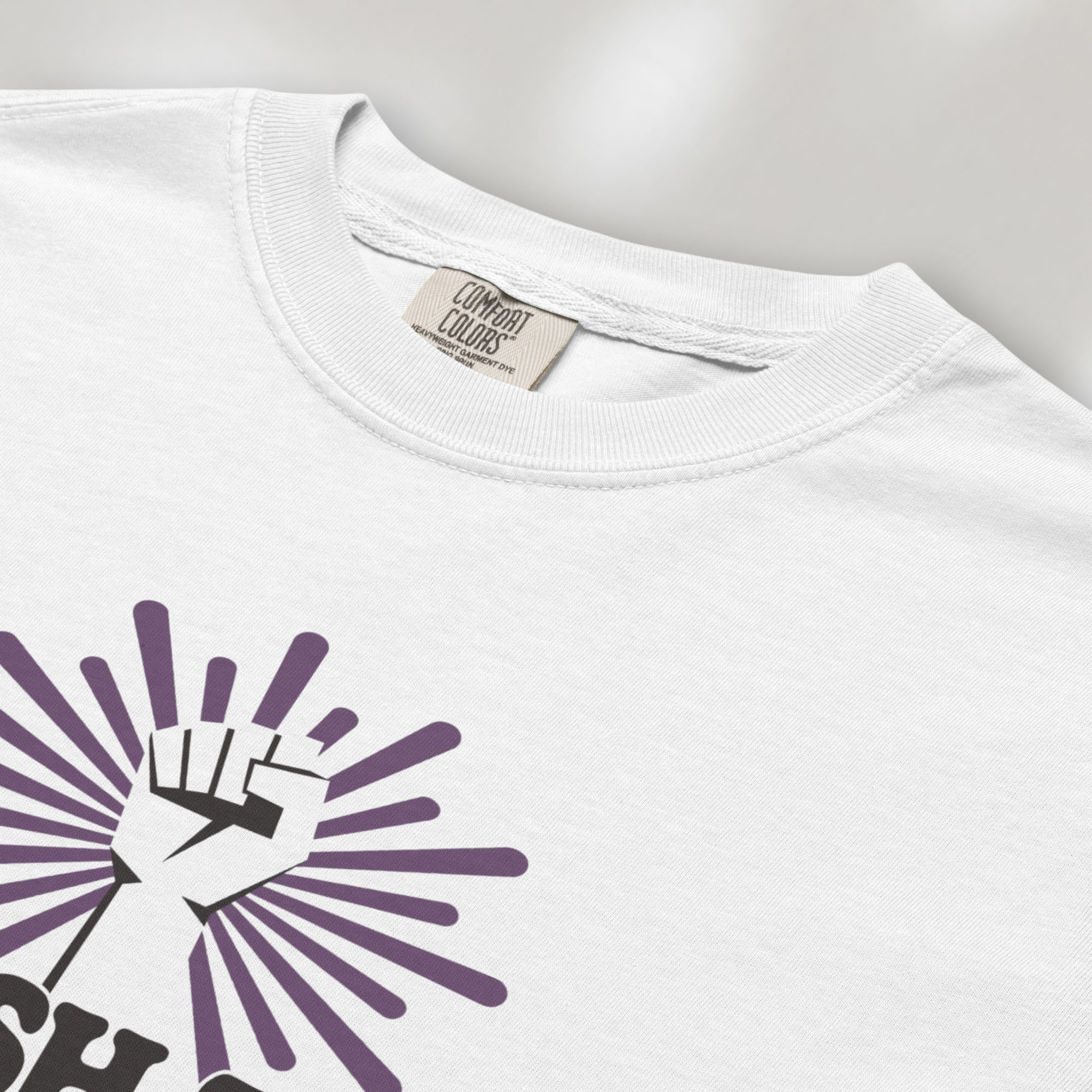 Closeup detail of white t-shirt with a raised fist graphic and purple burst above the text “Smash the Patriarchy.”
