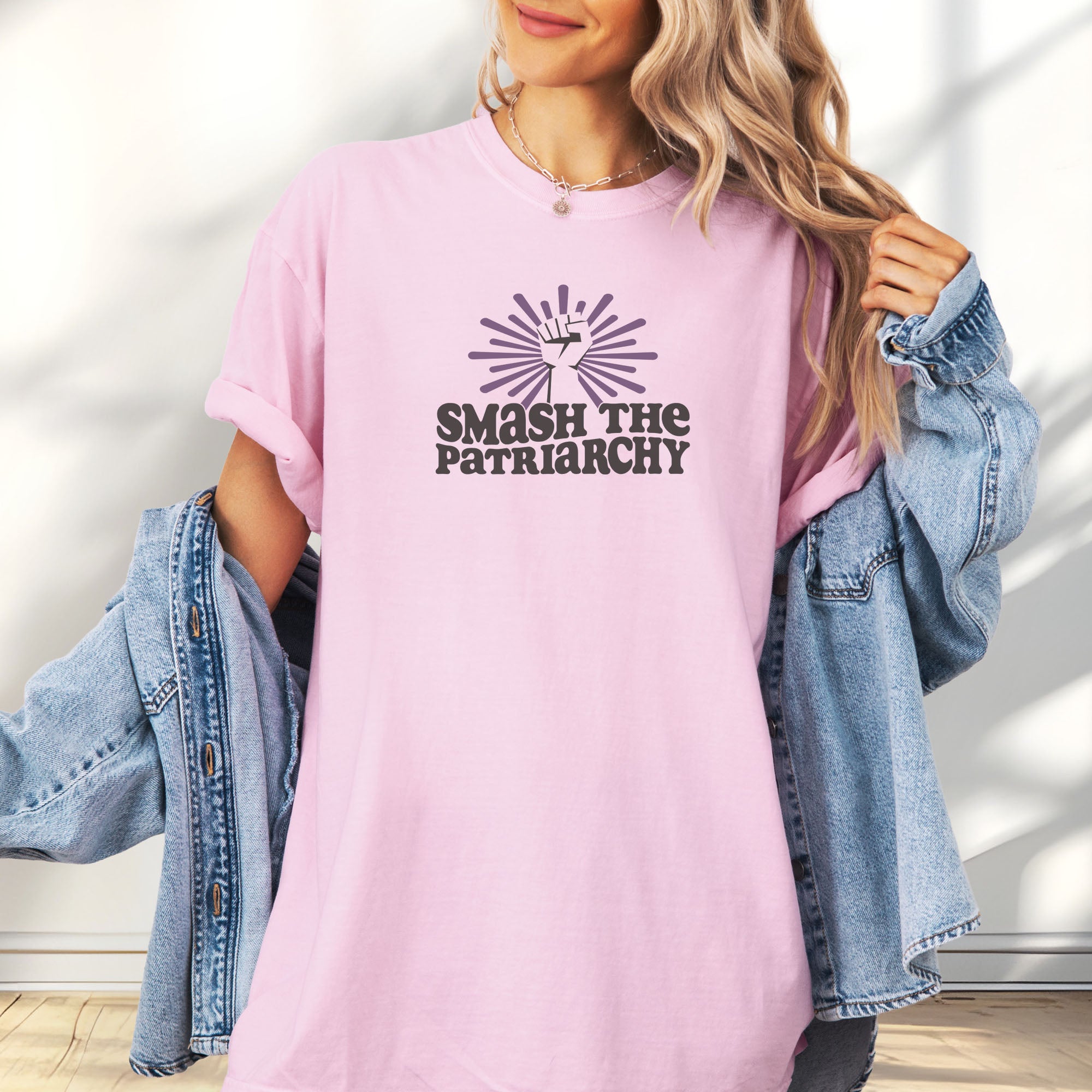 Female model wearing oversized blossom t-shirt with a raised fist graphic and purple burst above the text “Smash the Patriarchy.”