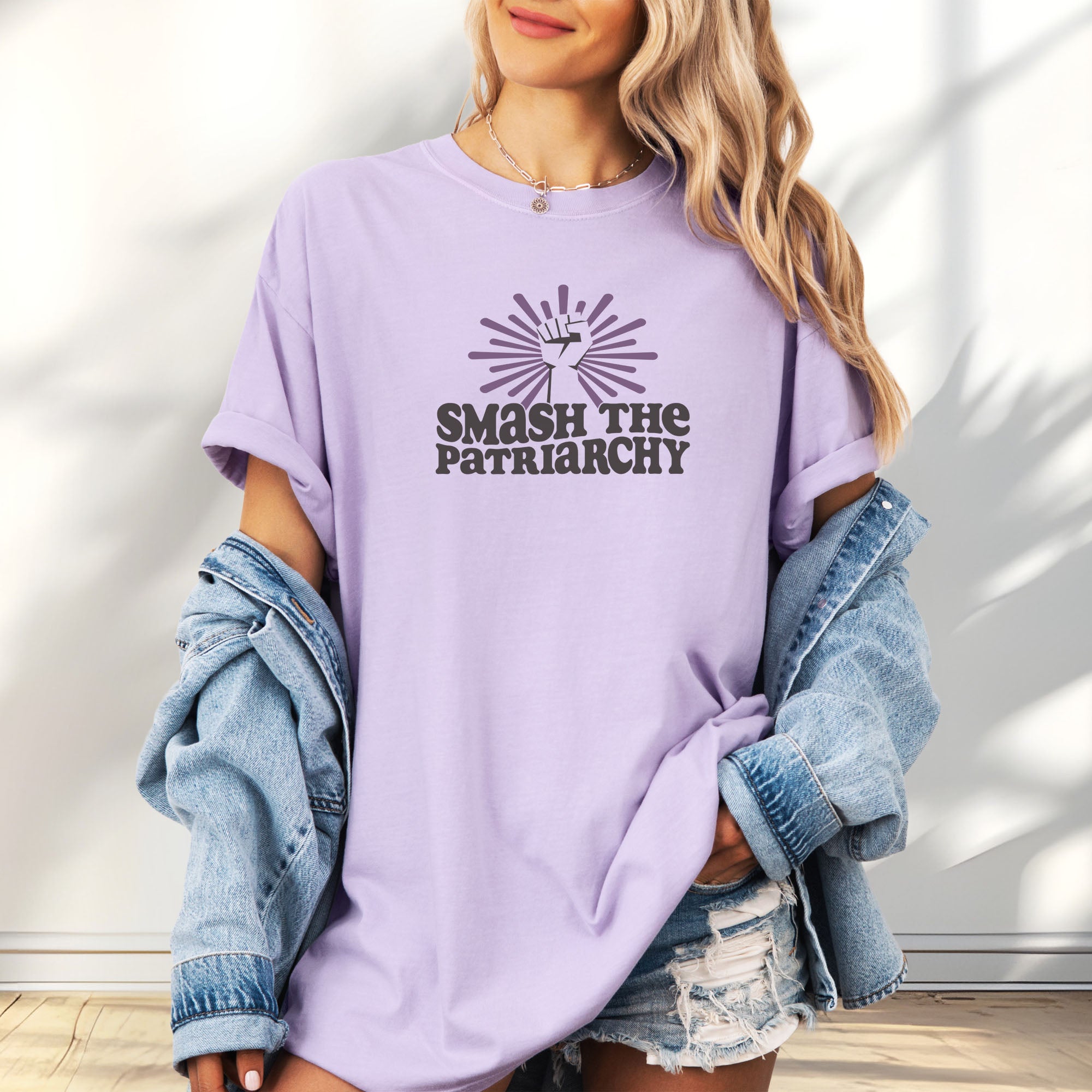 Female model wearing oversized orchid t-shirt with a raised fist graphic and purple burst above the text “Smash the Patriarchy.”