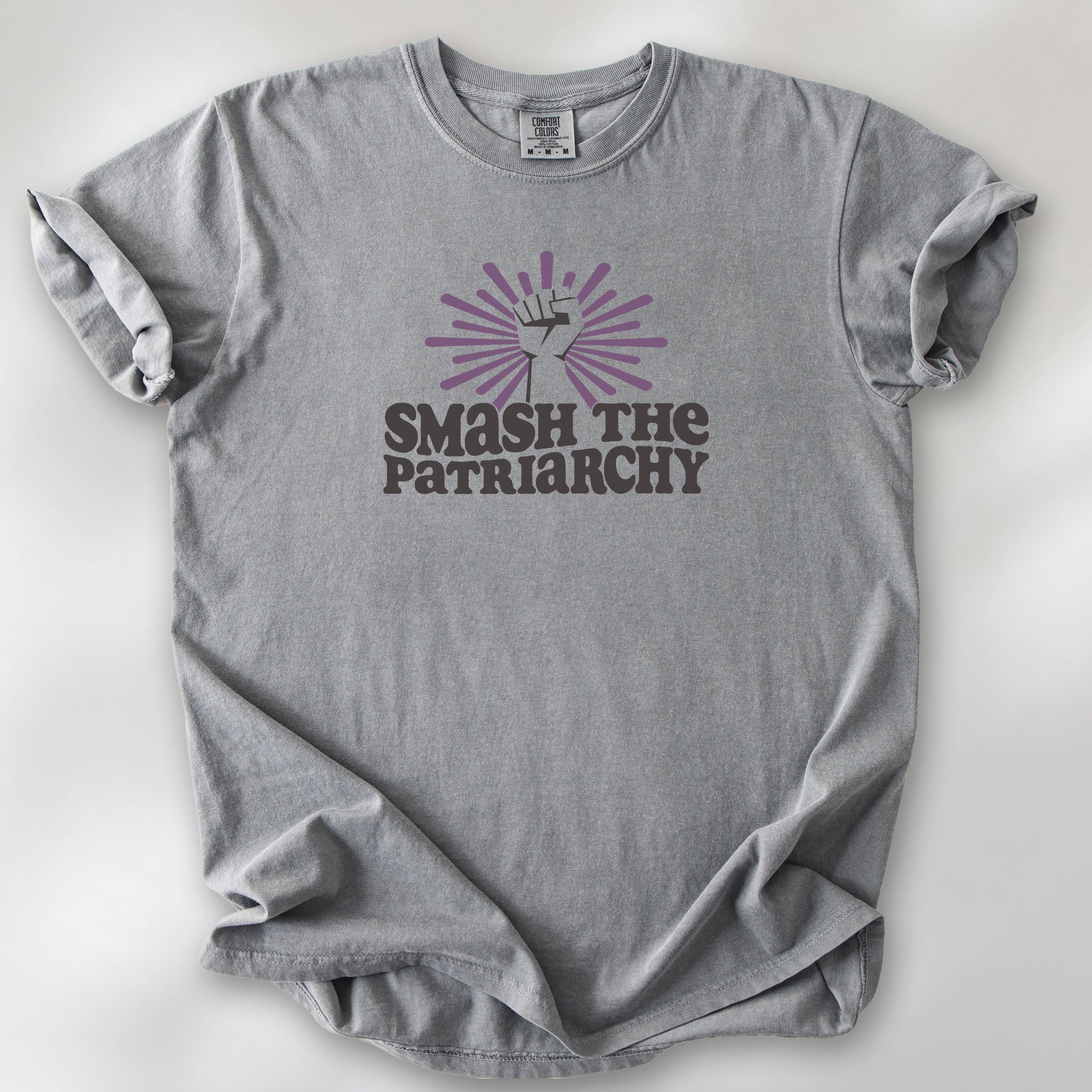 Grey t-shirt with a raised fist graphic and purple burst above the text “Smash the Patriarchy.”
