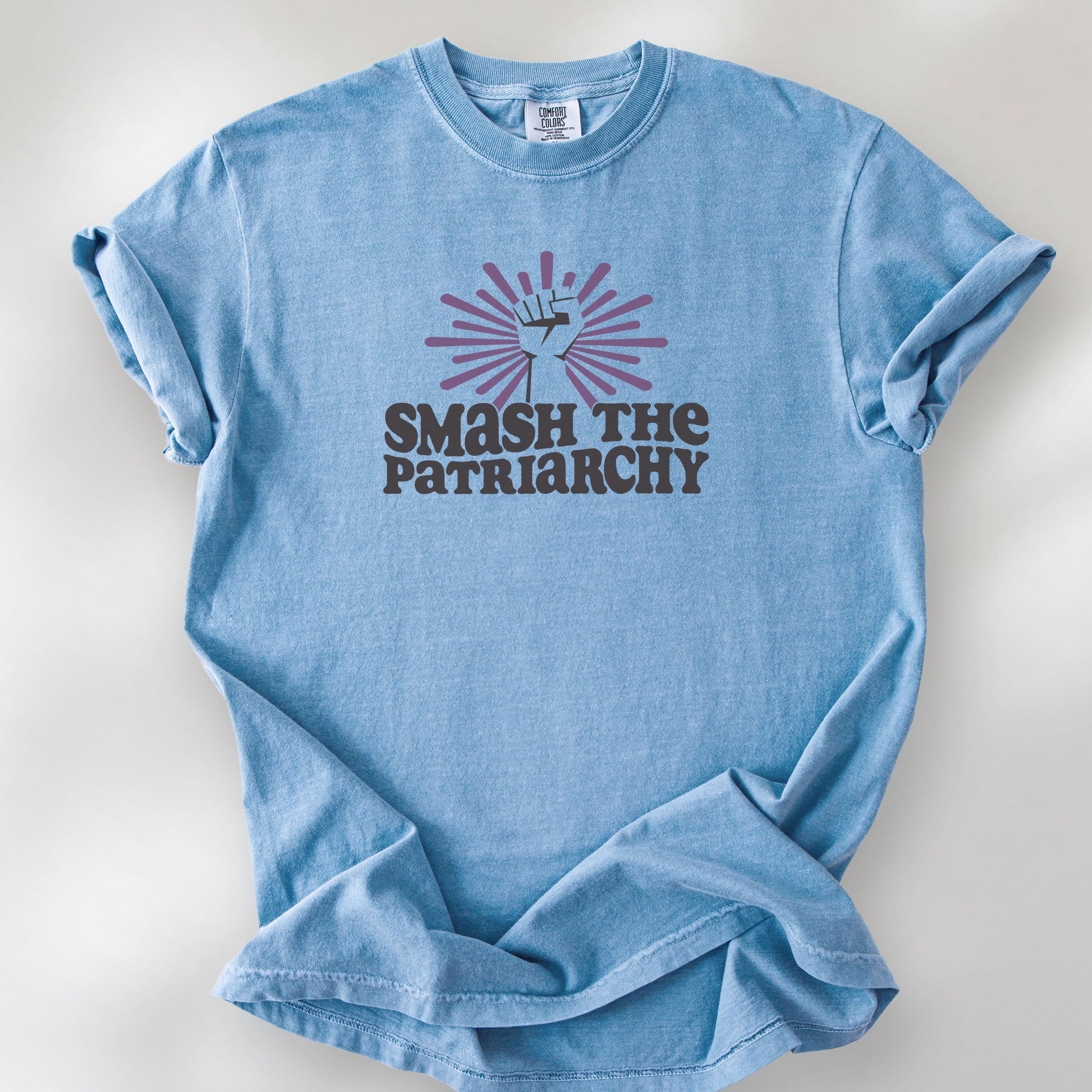 Washed denim t-shirt with a raised fist graphic and purple burst above the text “Smash the Patriarchy.”