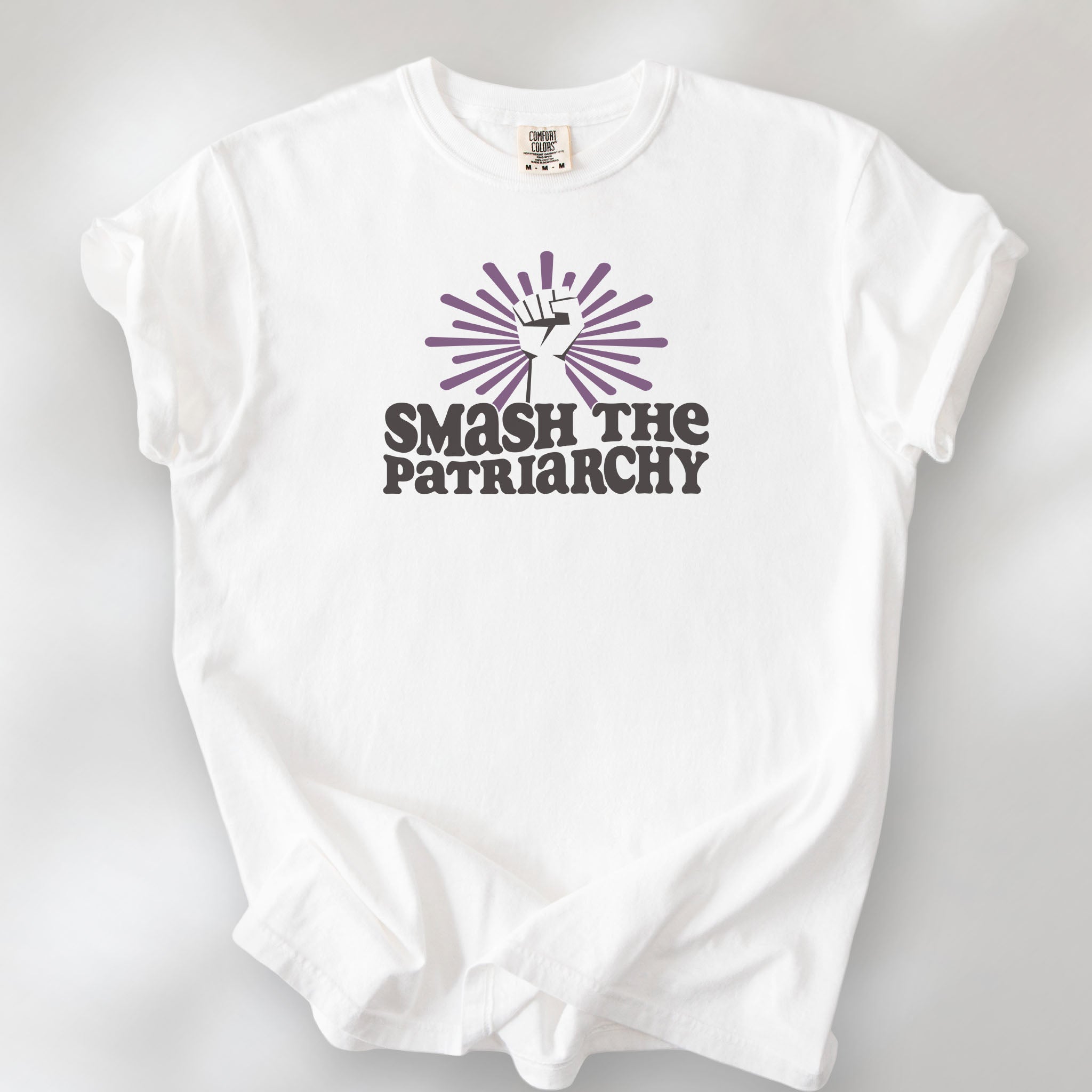 White t-shirt with a raised fist graphic and purple burst above the text “Smash the Patriarchy.”