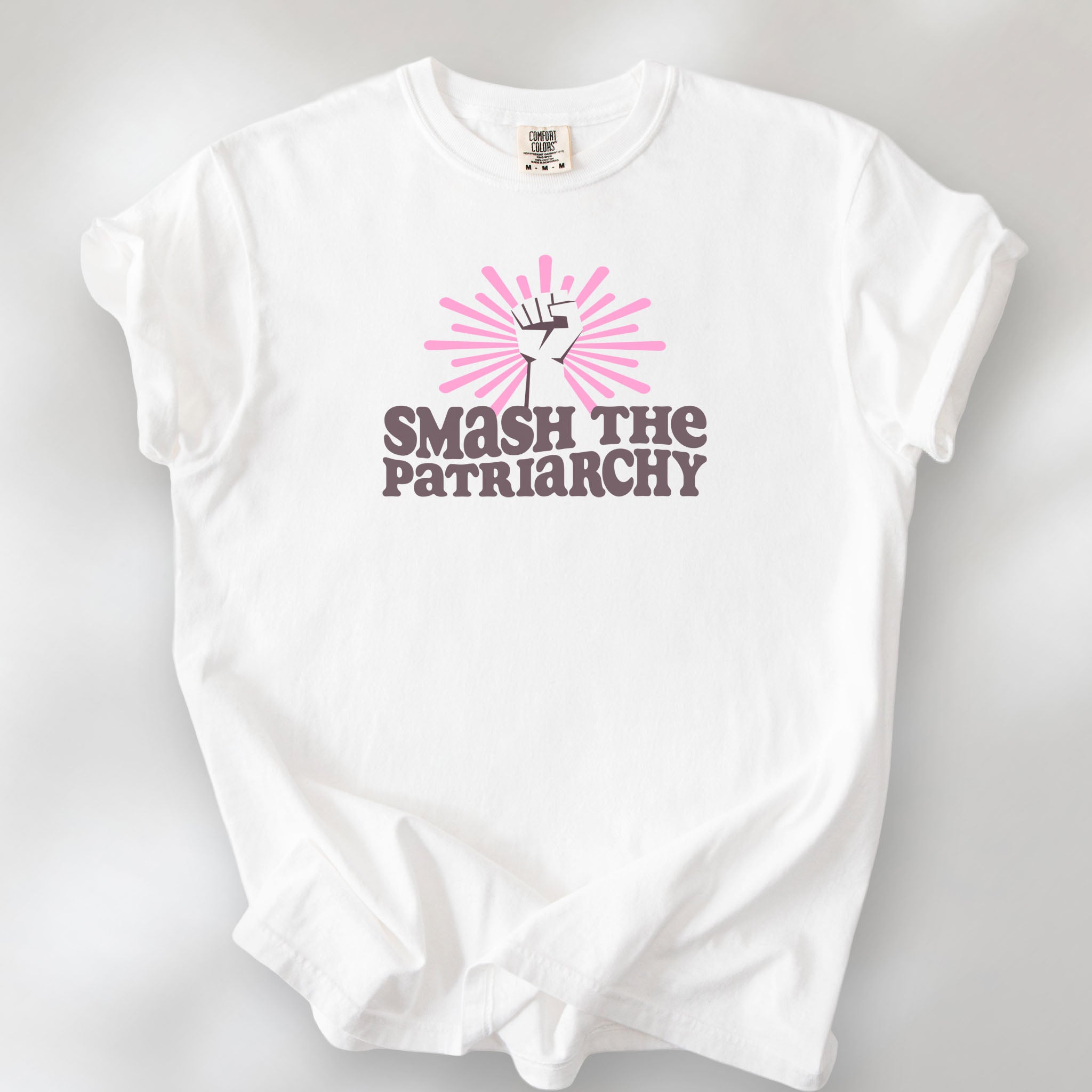 White t-shirt with a raised fist graphic and pink rays behind it, featuring the text “Smash the Patriarchy.”