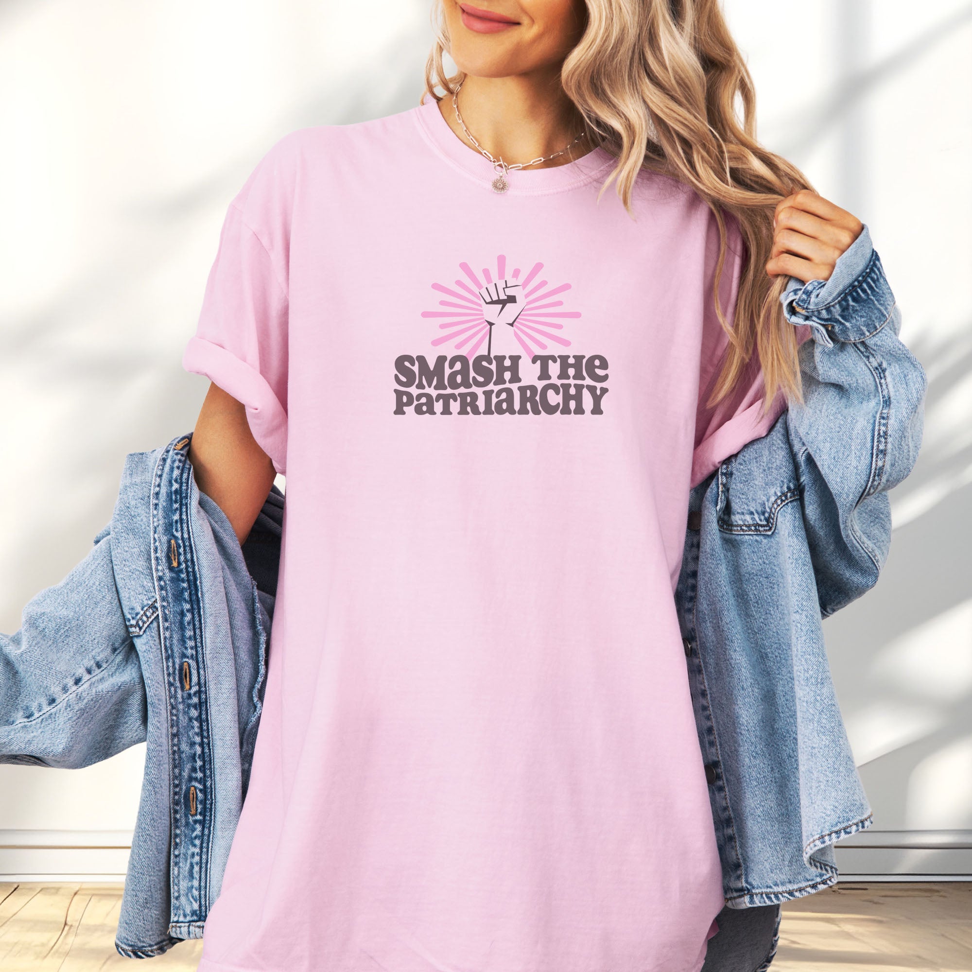 Female model wearing oversized blossom pink t-shirt with a raised fist graphic and pink rays behind it, featuring the text “Smash the Patriarchy.”