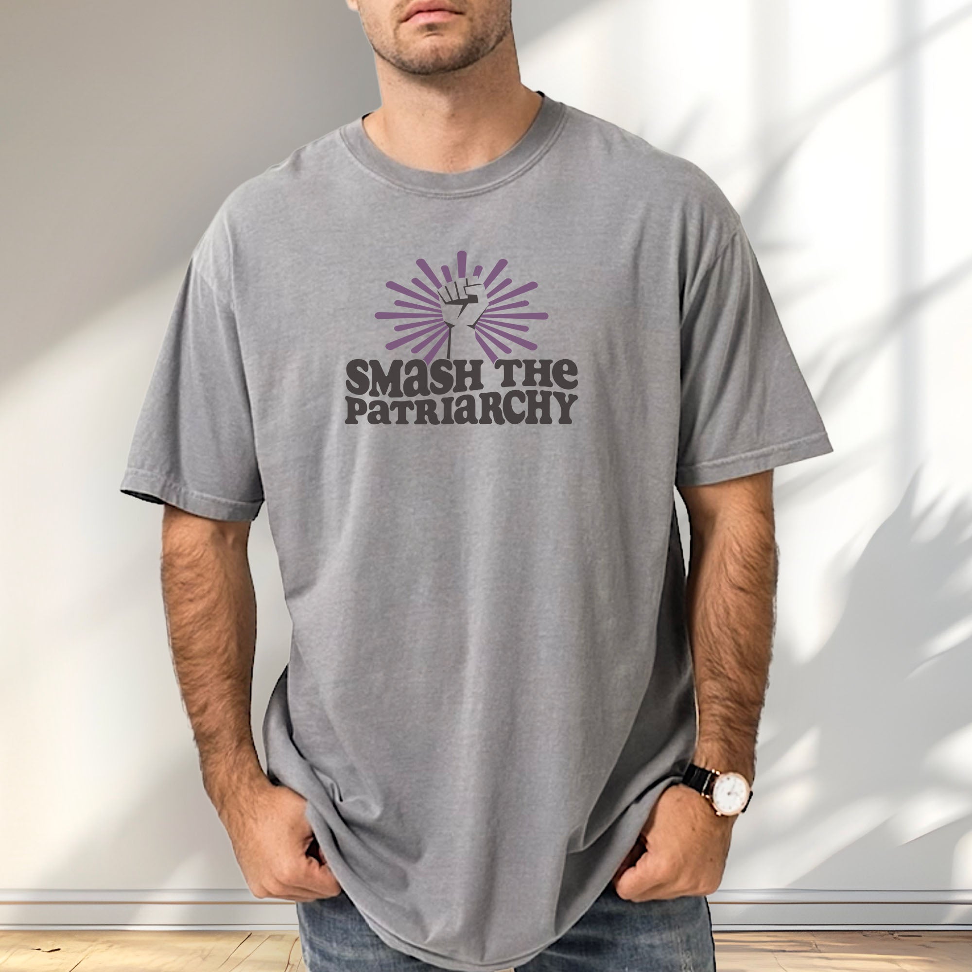 Male model wearing grey t-shirt with a raised fist graphic and purple burst above the text “Smash the Patriarchy.”