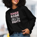 Female model wearing black protest sweatshirt with bold pink and grey text reading “rage rage against the dying of your rights” – feminist anti-trump activist shirt.