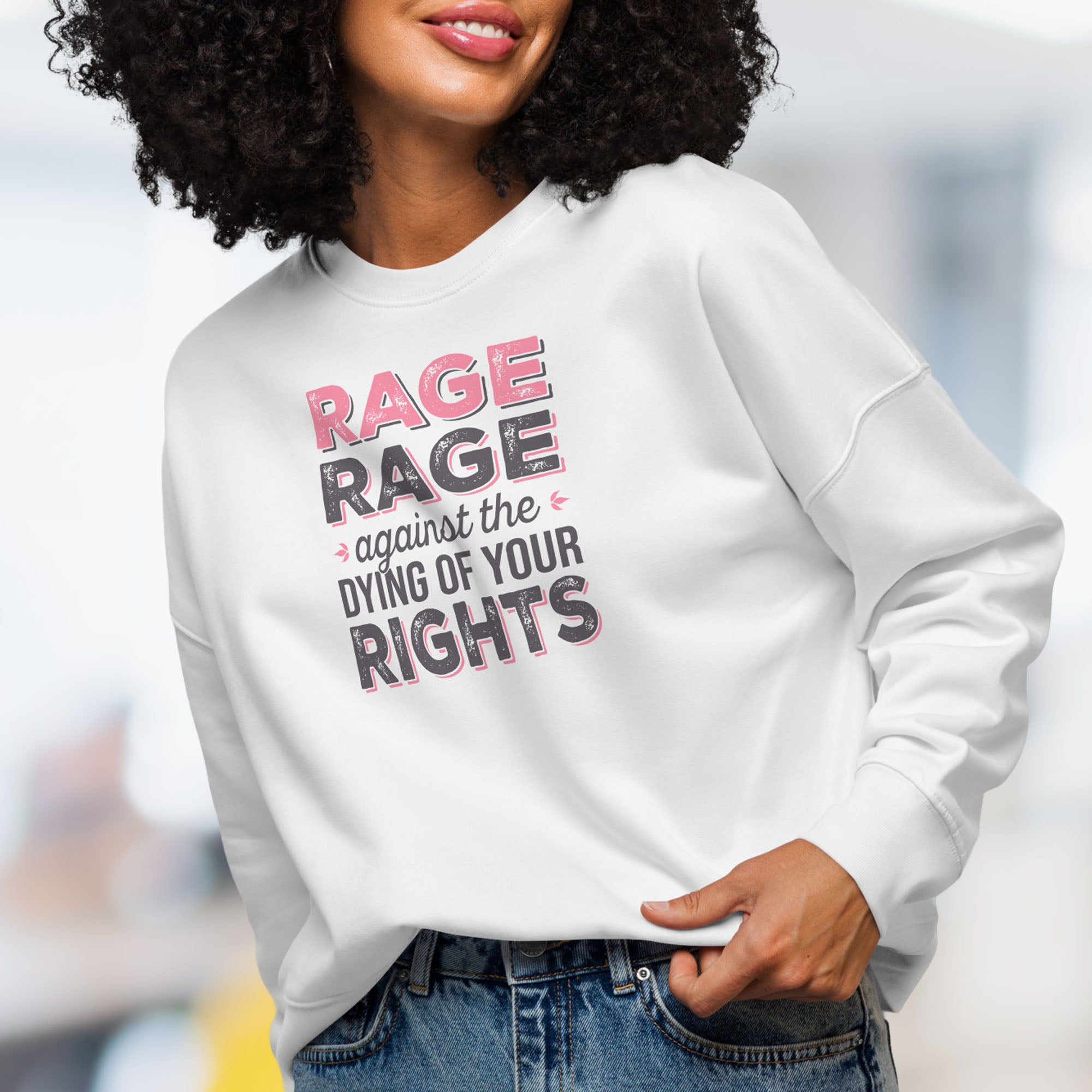 Female model wearing white protest sweatshirt with bold pink and grey text reading “rage rage against the dying of your rights” – feminist anti-trump activist shirt.