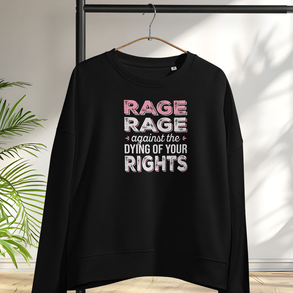Black women's protest sweatshirt with bold pink and grey text reading “rage rage against the dying of your rights” – feminist anti-trump activist shirt, hanging on a hanger.