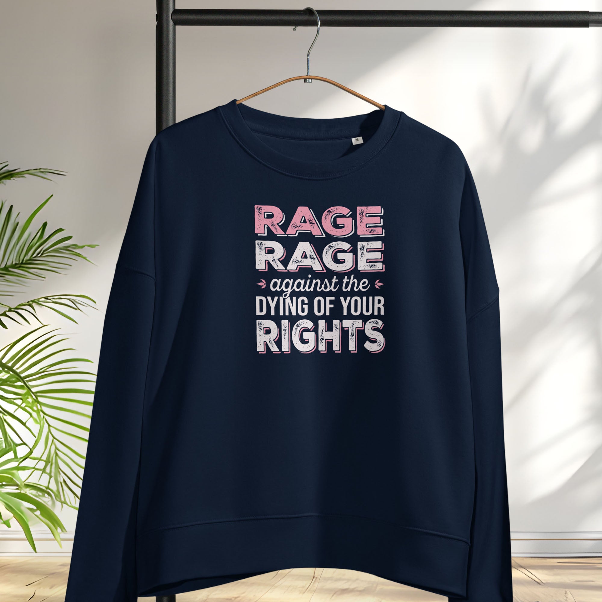 Navy women's protest sweatshirt with bold pink and grey text reading “rage rage against the dying of your rights” – feminist anti-trump activist shirt, hanging on a hanger.
