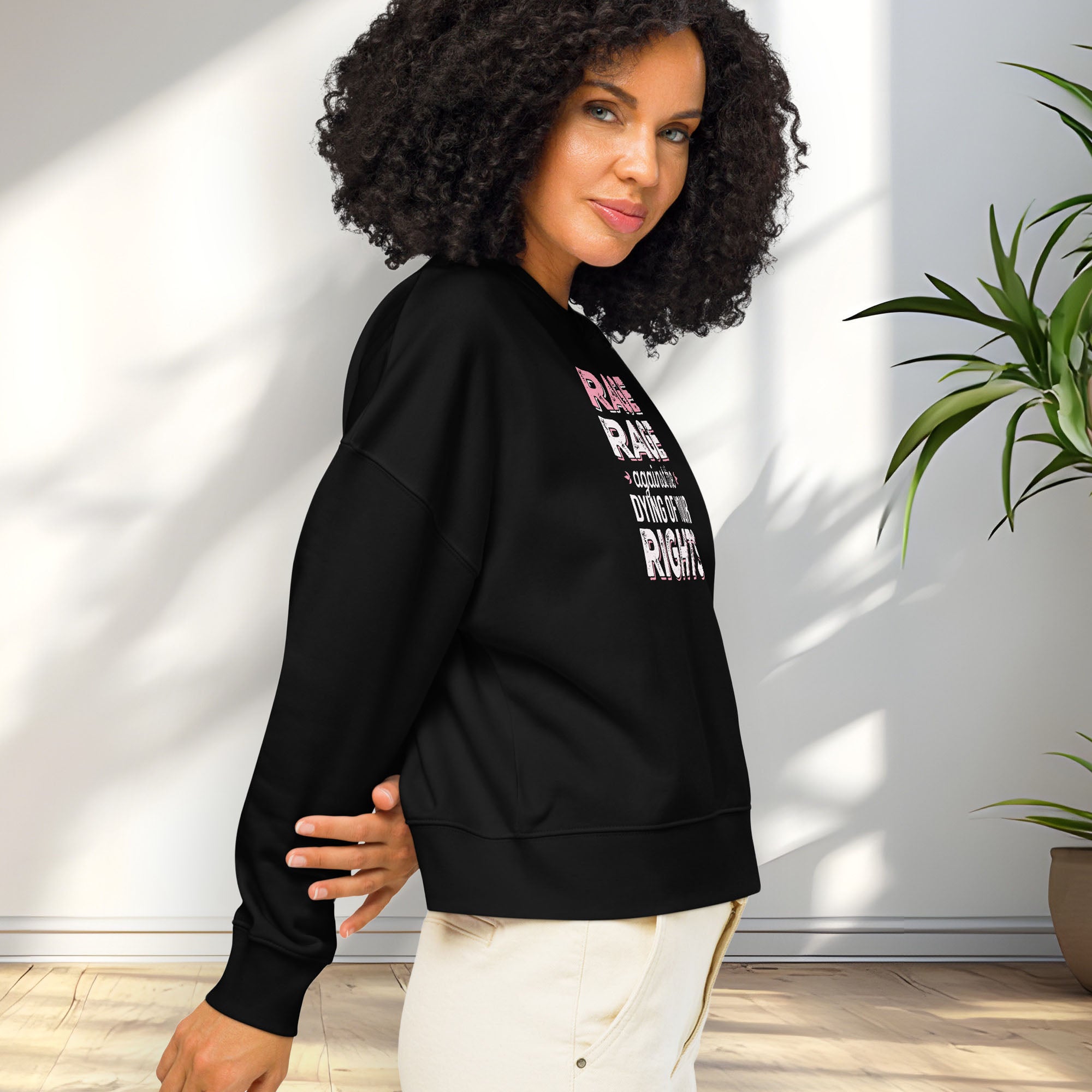 Side view of female model wearing black protest sweatshirt with bold pink and grey text reading “rage rage against the dying of your rights” – feminist anti-trump activist shirt.