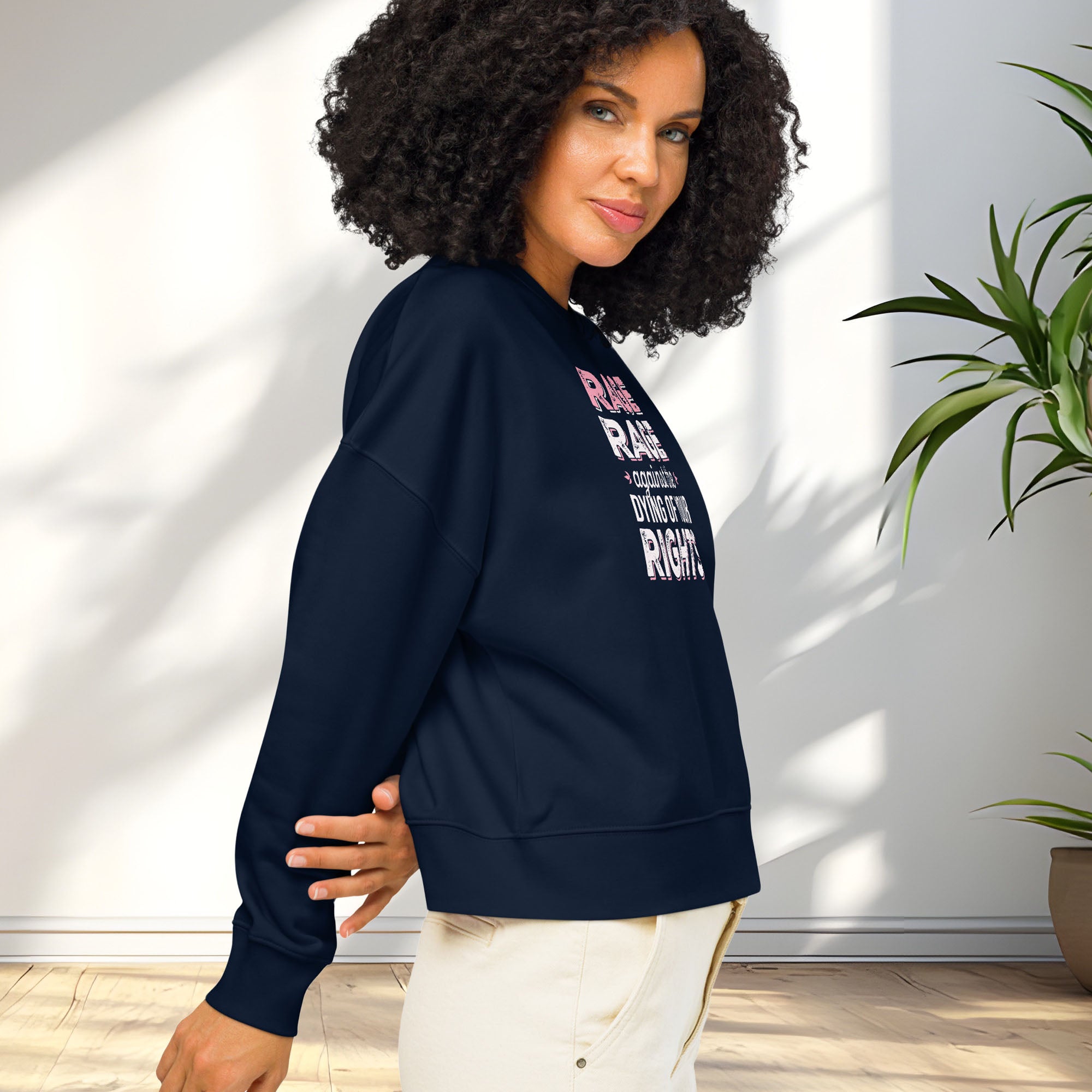 Side view of female model wearing navy protest sweatshirt with bold pink and grey text reading “rage rage against the dying of your rights” – feminist anti-trump activist shirt.
