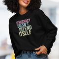 Female model wearing women's black sweatshirt with bright pink, blue, green, and yellow bold text that says "democracy doesn't defend itself."