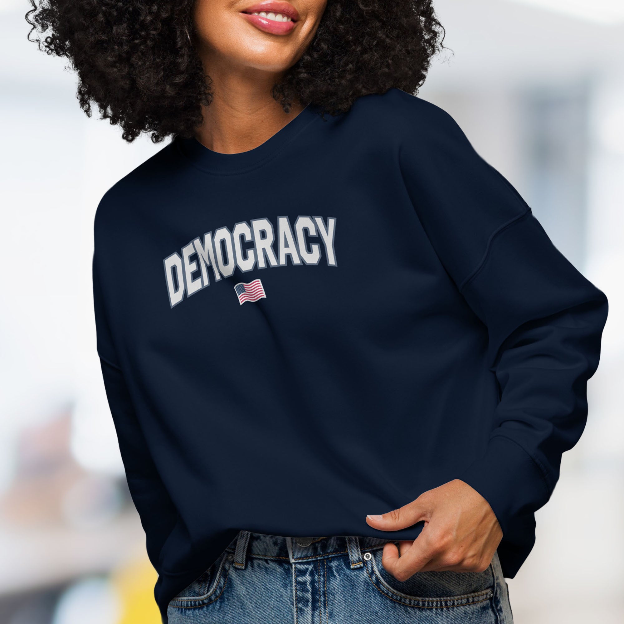 Front view of female model wearing women's navy sweatshirt with the word “Democracy” in bold grey letters and a small American flag underneath, symbolizing U.S. pride in democracy over authoritarianism, tyranny, dictators.
