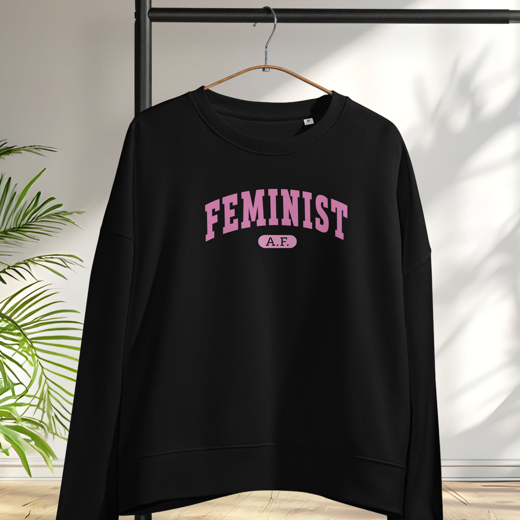 Hanging black sweatshirt with pink text that reads “Feminist A.F.” in a collegiate style.