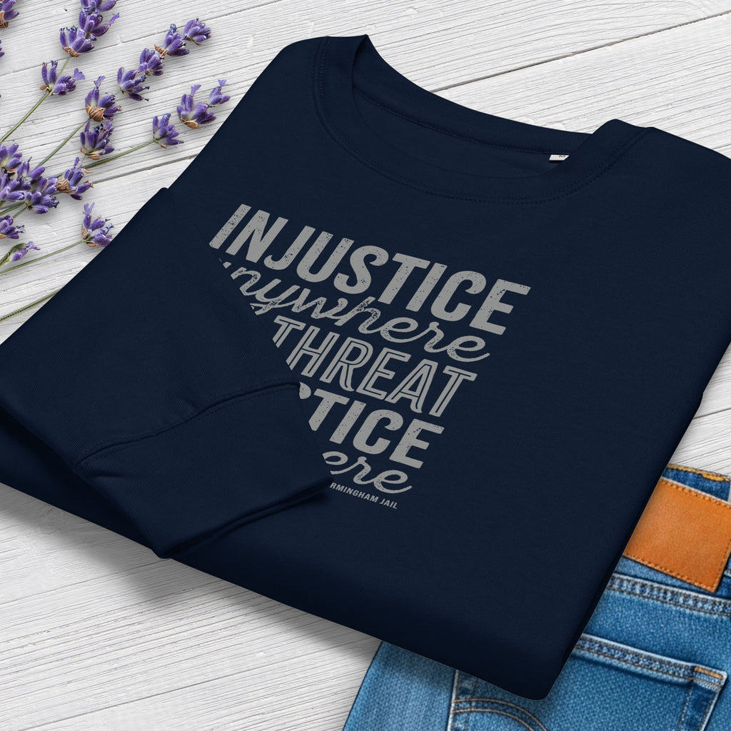 Folded navy sweatshirt with bold text reading “Injustice anywhere is a threat to justice everywhere” quote from Martin Luther King Jr, MLK Jr, Letters from Birmingham jail — civil rights protest apparel for activists. Styled with jeans and flowers.