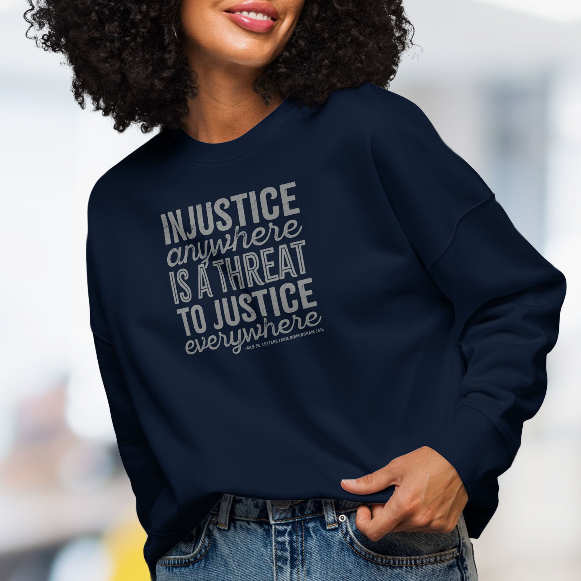 Front view of female model wearing navy sweatshirt with bold text reading “Injustice anywhere is a threat to justice everywhere” quote from Martin Luther King Jr, MLK Jr, Letters from Birmingham jail — civil rights protest apparel for activists.