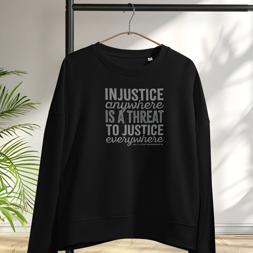 Black sweatshirt with bold text reading “Injustice anywhere is a threat to justice everywhere” quote from Martin Luther King Jr, MLK Jr, Letters from Birmingham jail — civil rights protest apparel for activists. Hanging on a hanger.