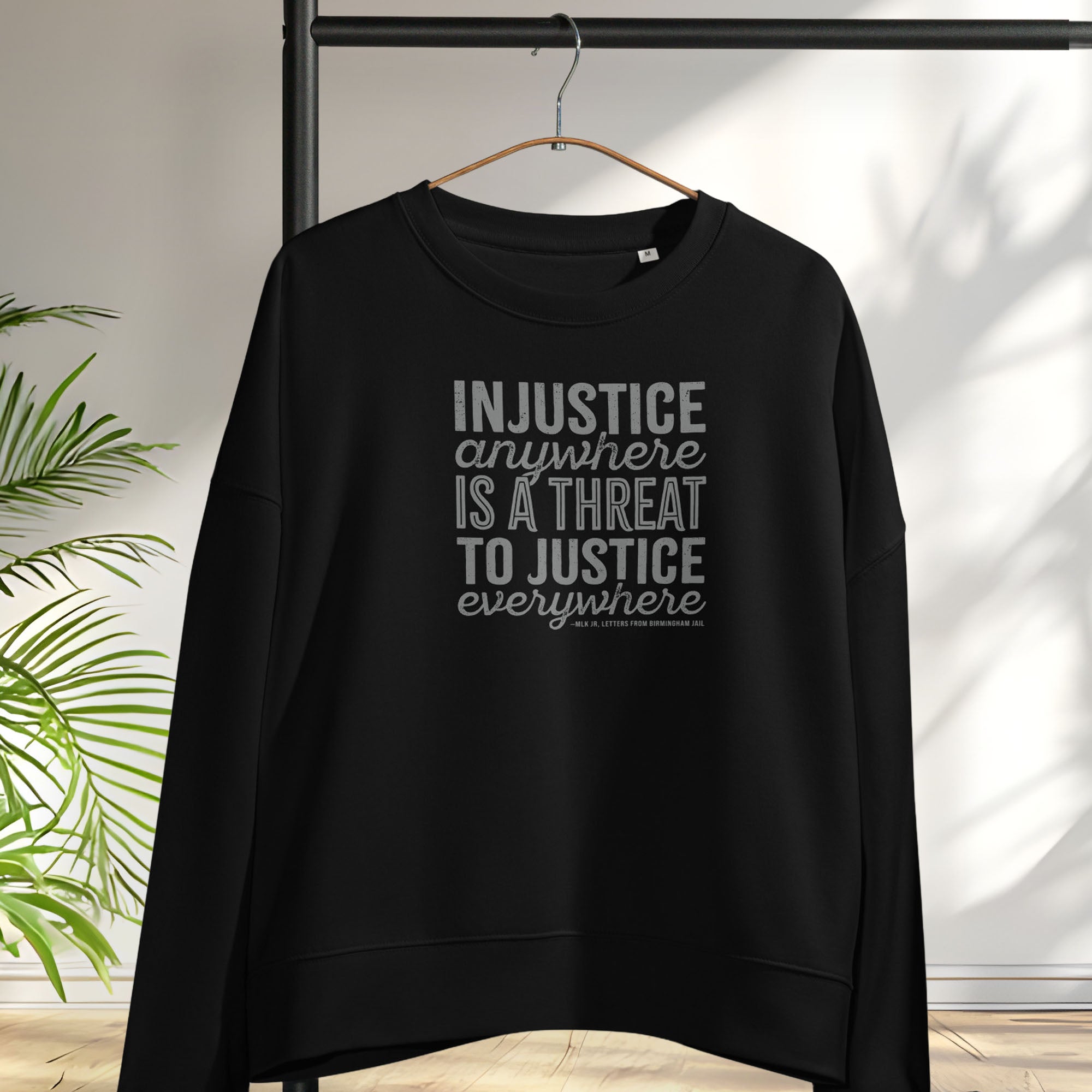 Black sweatshirt with bold text reading “Injustice anywhere is a threat to justice everywhere” quote from Martin Luther King Jr, MLK Jr, Letters from Birmingham jail — civil rights protest apparel for activists. Hanging on a hanger.