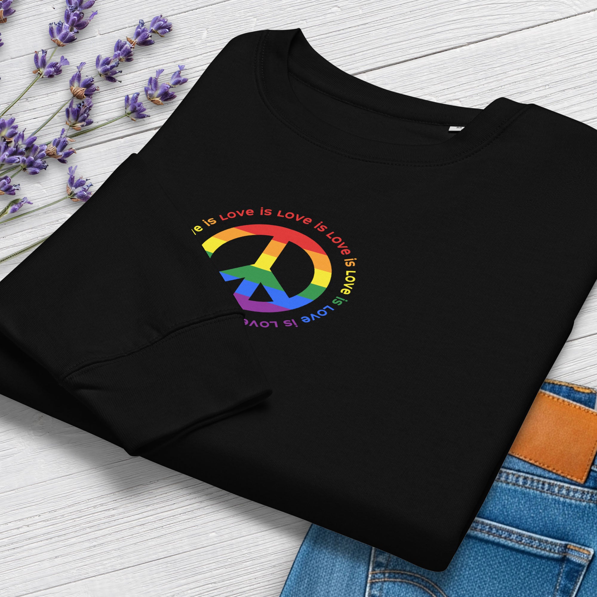 Folded black sweatshirt with LGBTQ pride graphic — a peace sign in the LGBTQ flag colors, with the text "love is love" repeated in a circle around the peace sign, showing cuff detail.