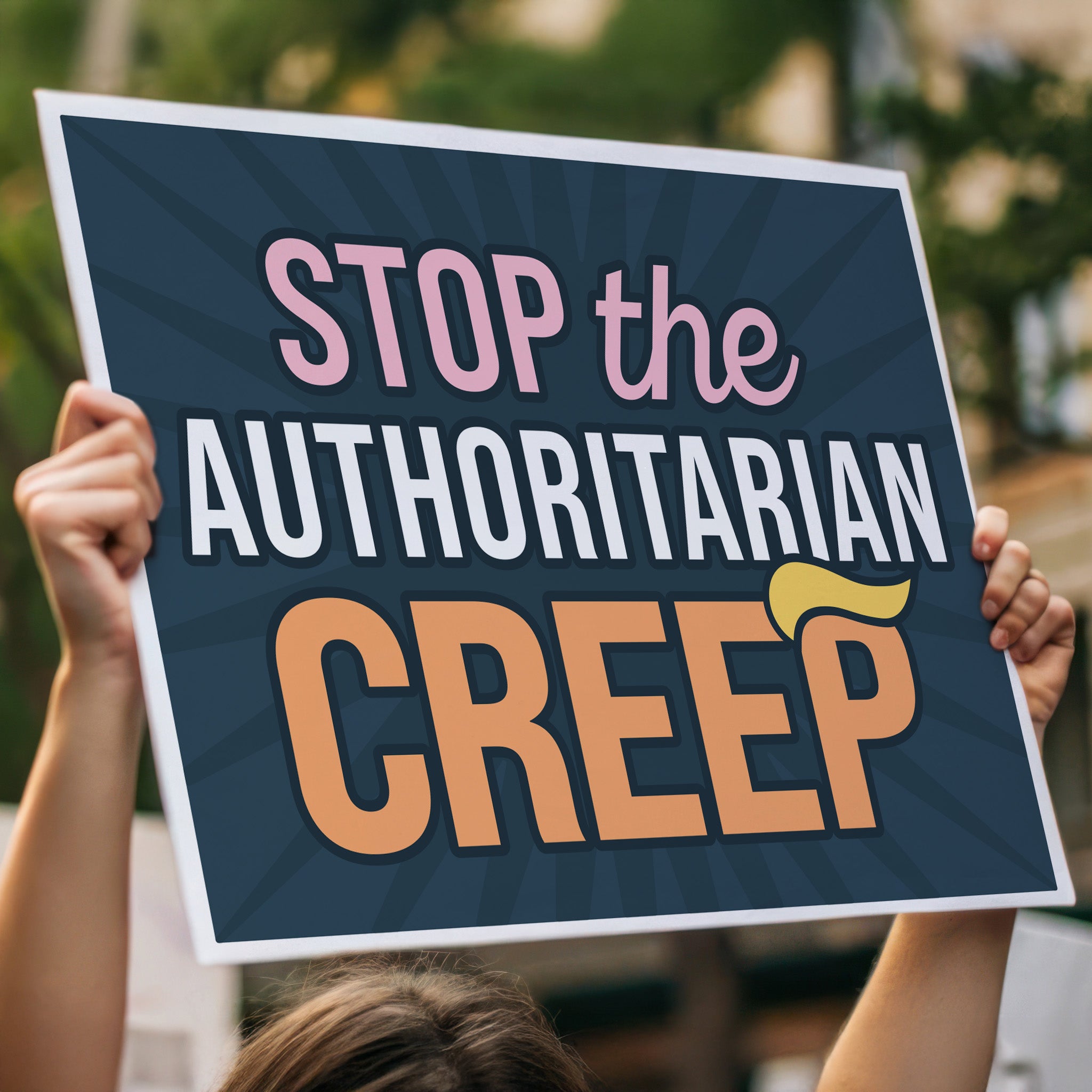 Person holding up rotest sign in a crowd with the phrase "Stop the Authoritarian Creep" in bold lettering, featuring a yellow hairpiece resembling Trump’s weird hair on the last letter of the word “Creep,” emphasizing the double meaning of the sign.