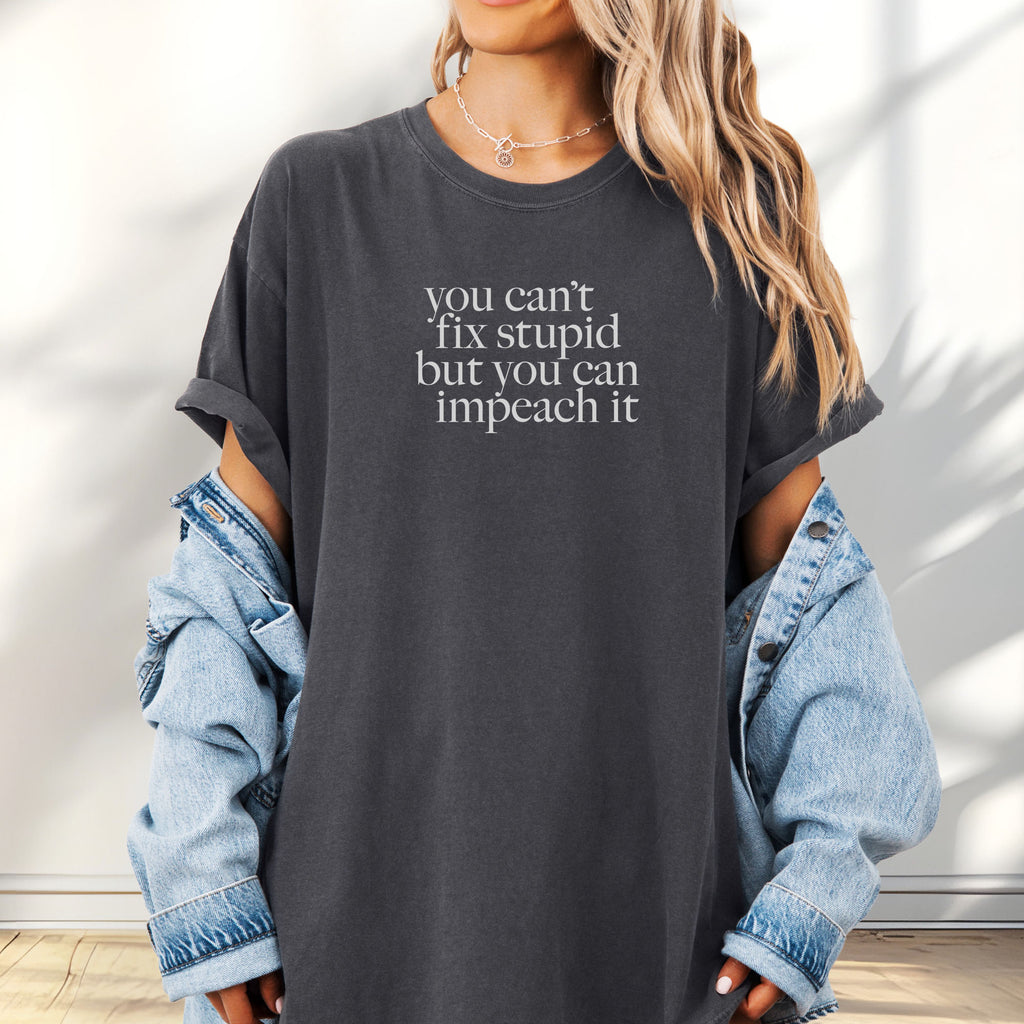 Female model wearing oversized pepper political t-shirt with serif text reading “You can’t fix stupid but you can impeach it.".