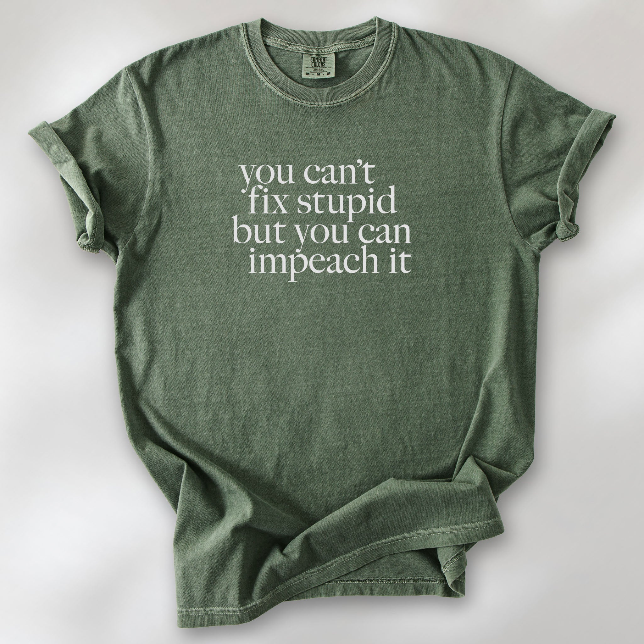 Moss political t-shirt with serif text reading “You can’t fix stupid but you can impeach it.".