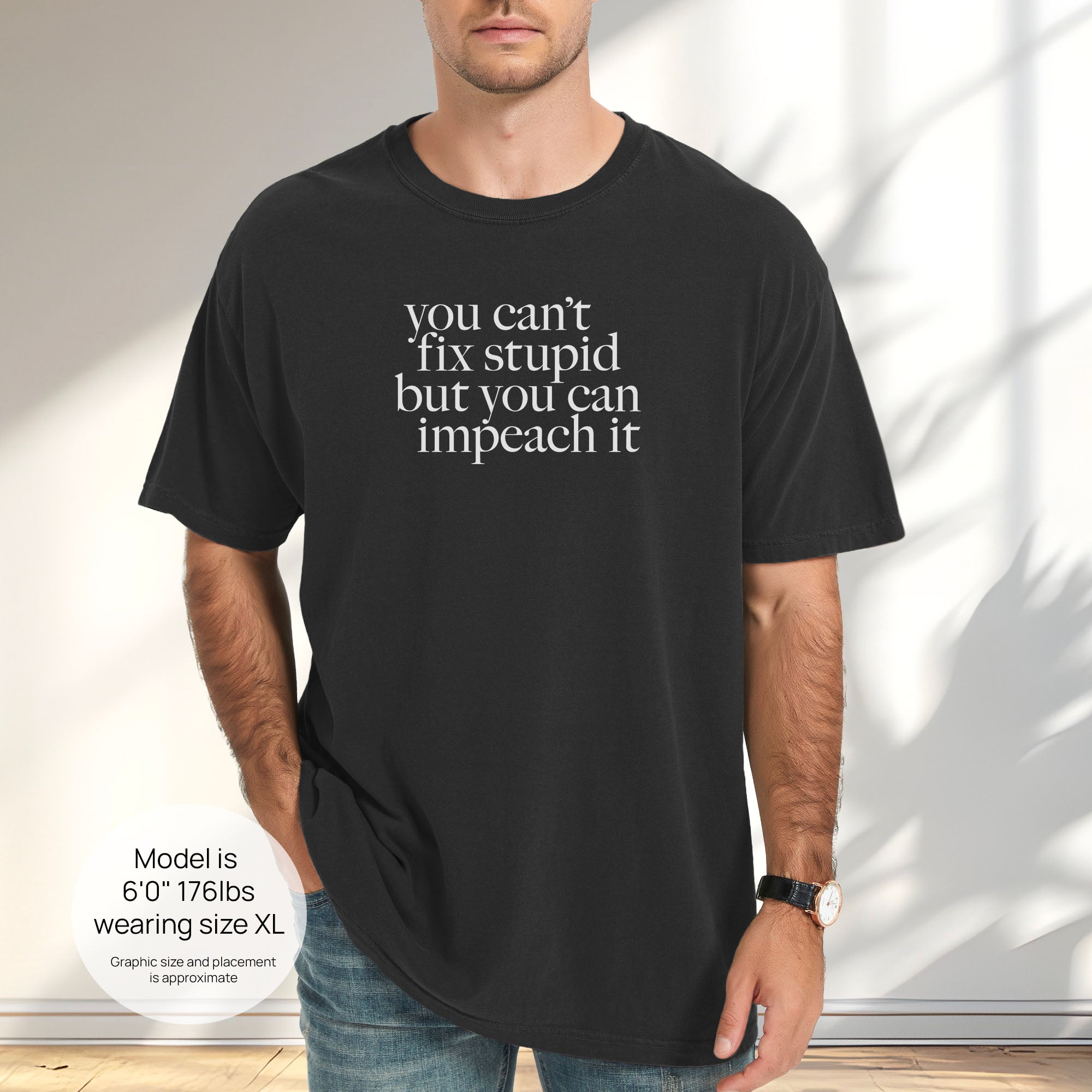 Male model wearing black political t-shirt with serif text reading “You can’t fix stupid but you can impeach it." Includes size and fit information for the model who is 6 feet 0 inches, 176 pounds, and wearing a size XL shirt.
