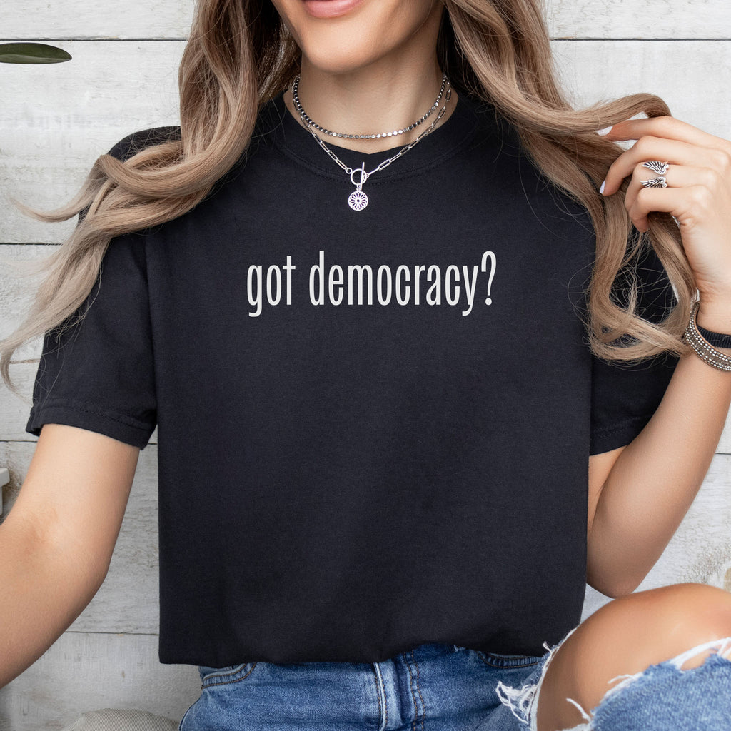 Female model wearing black t-shirt with white text reading “got democracy?” in minimalist font, styled like the classic “got milk?” campaign design.
