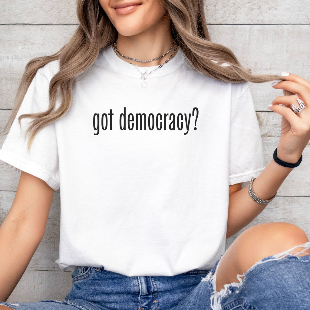Female model wearing white t-shirt with black text reading “got democracy?” in minimalist font, styled like the classic “got milk?” campaign design.