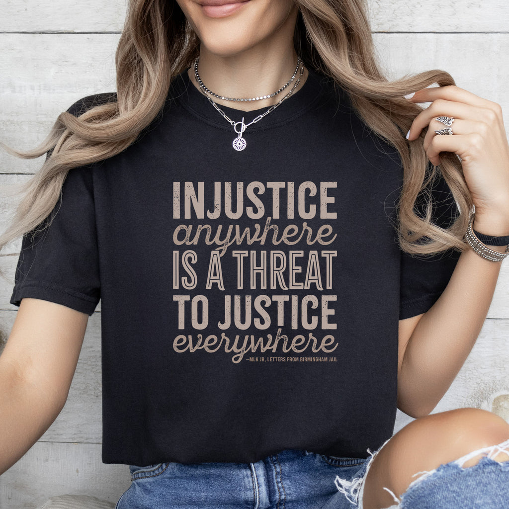 Female model wearing black t-shirt with bold text reading “Injustice anywhere is a threat to justice everywhere” quote from Martin Luther King Jr, MLK Jr, Letters from Birmingham jail — civil rights protest apparel for activists.