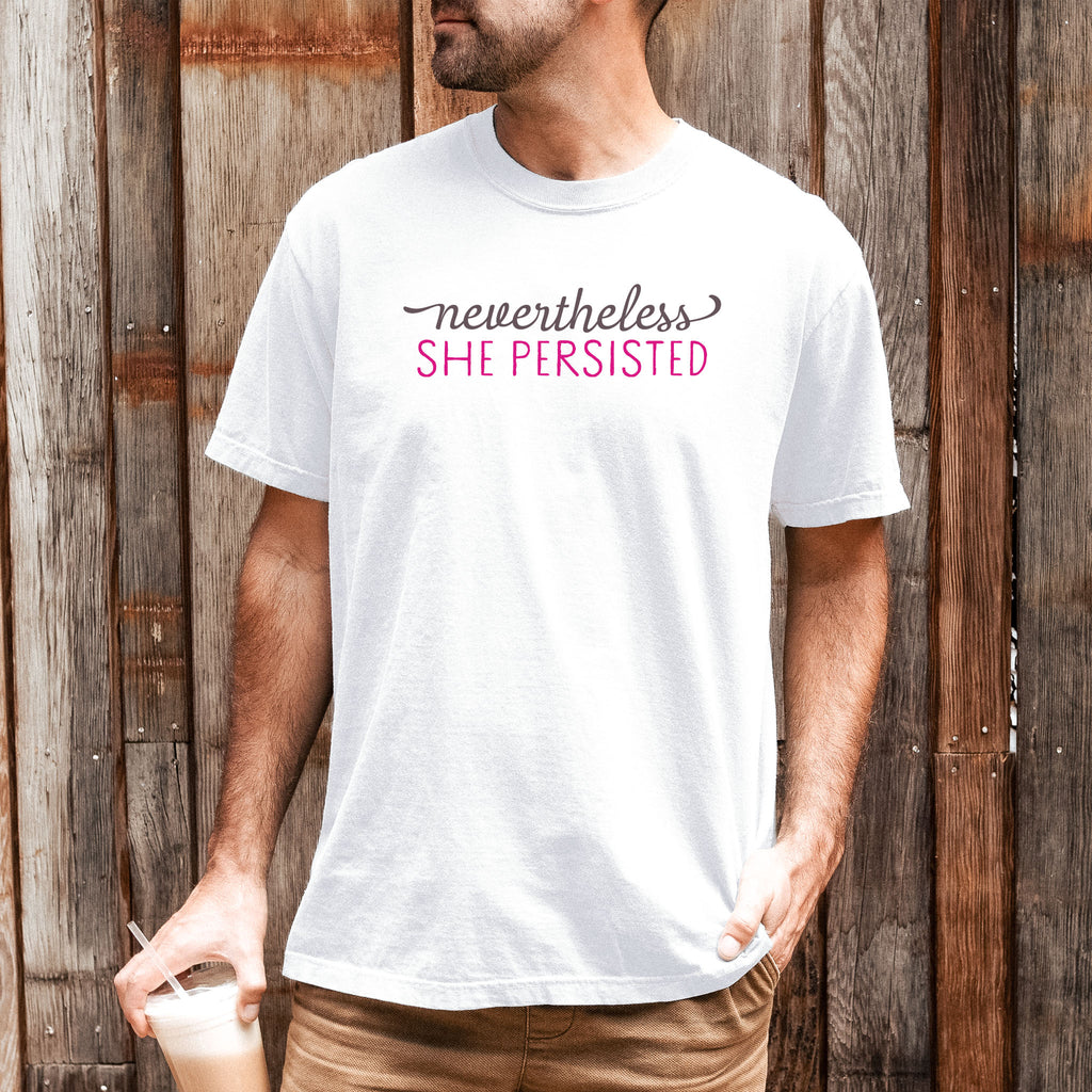 Male model wearing white Comfort Colors garment-dyed tee with stylized text graphic that reads "nevertheless she persisted."