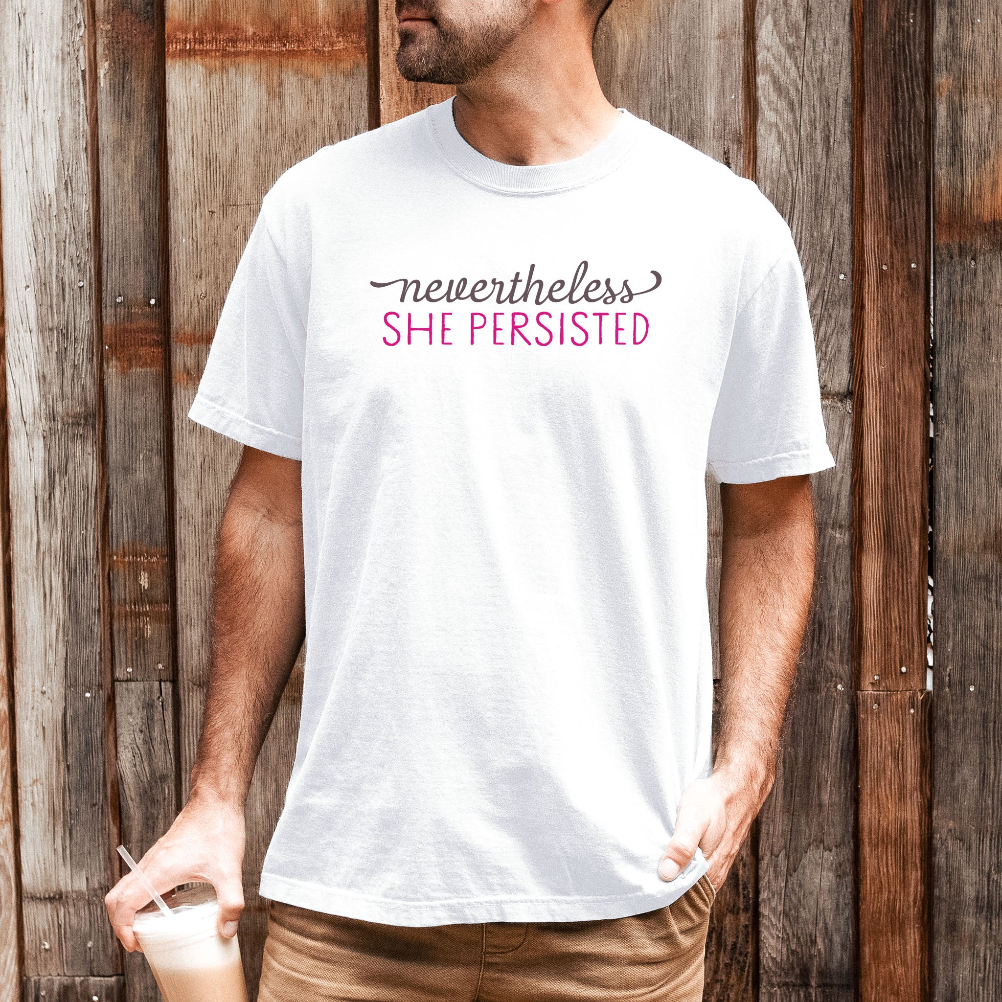 Male model wearing white Comfort Colors garment-dyed tee with stylized text graphic that reads "nevertheless she persisted."