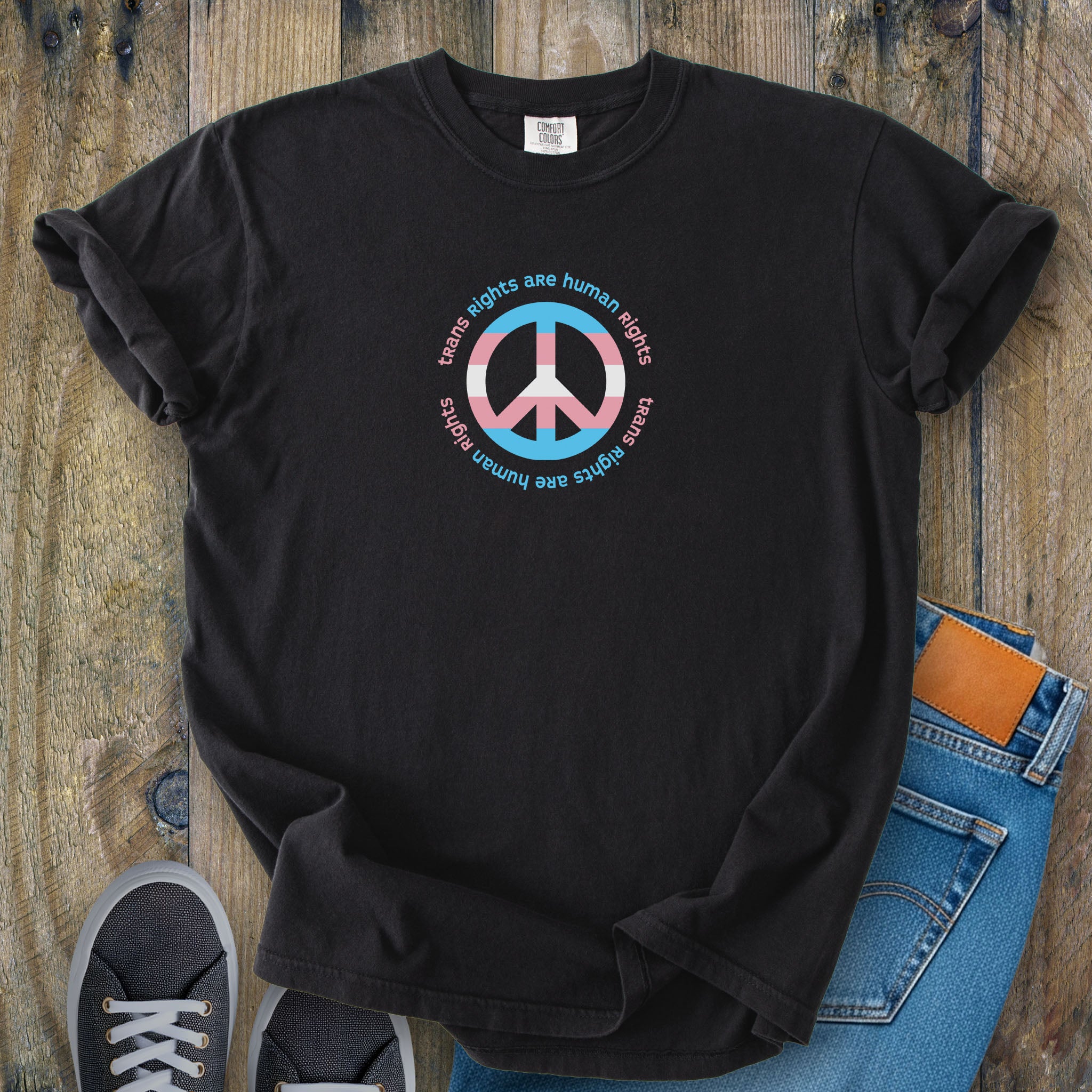 Black t-shirt with a peace sign in transgender flag colors and the text “Trans Rights Are Human Rights” in a circular design.