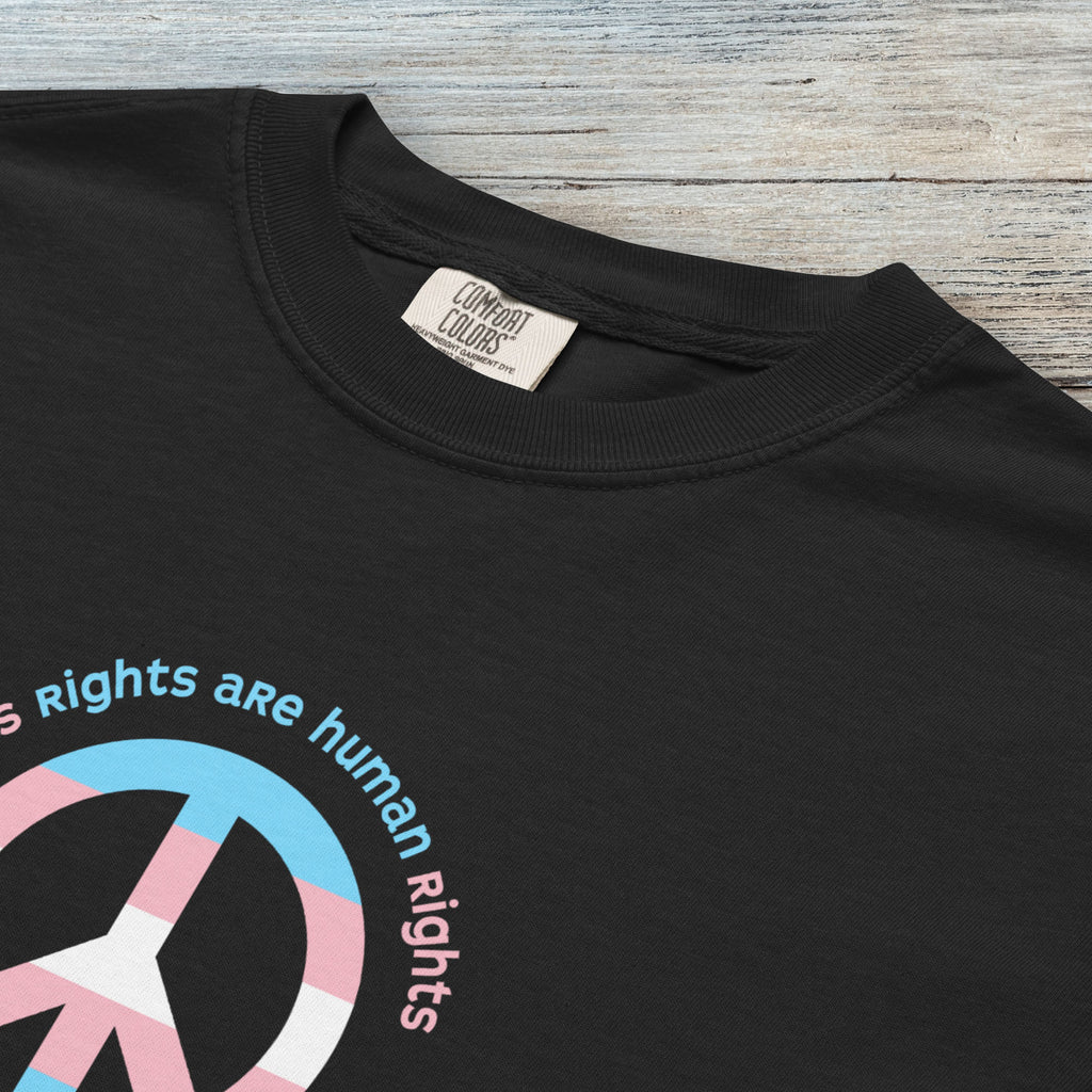 Closeup detail of black t-shirt with a peace sign in transgender flag colors and the text “Trans Rights Are Human Rights” in a circular design.