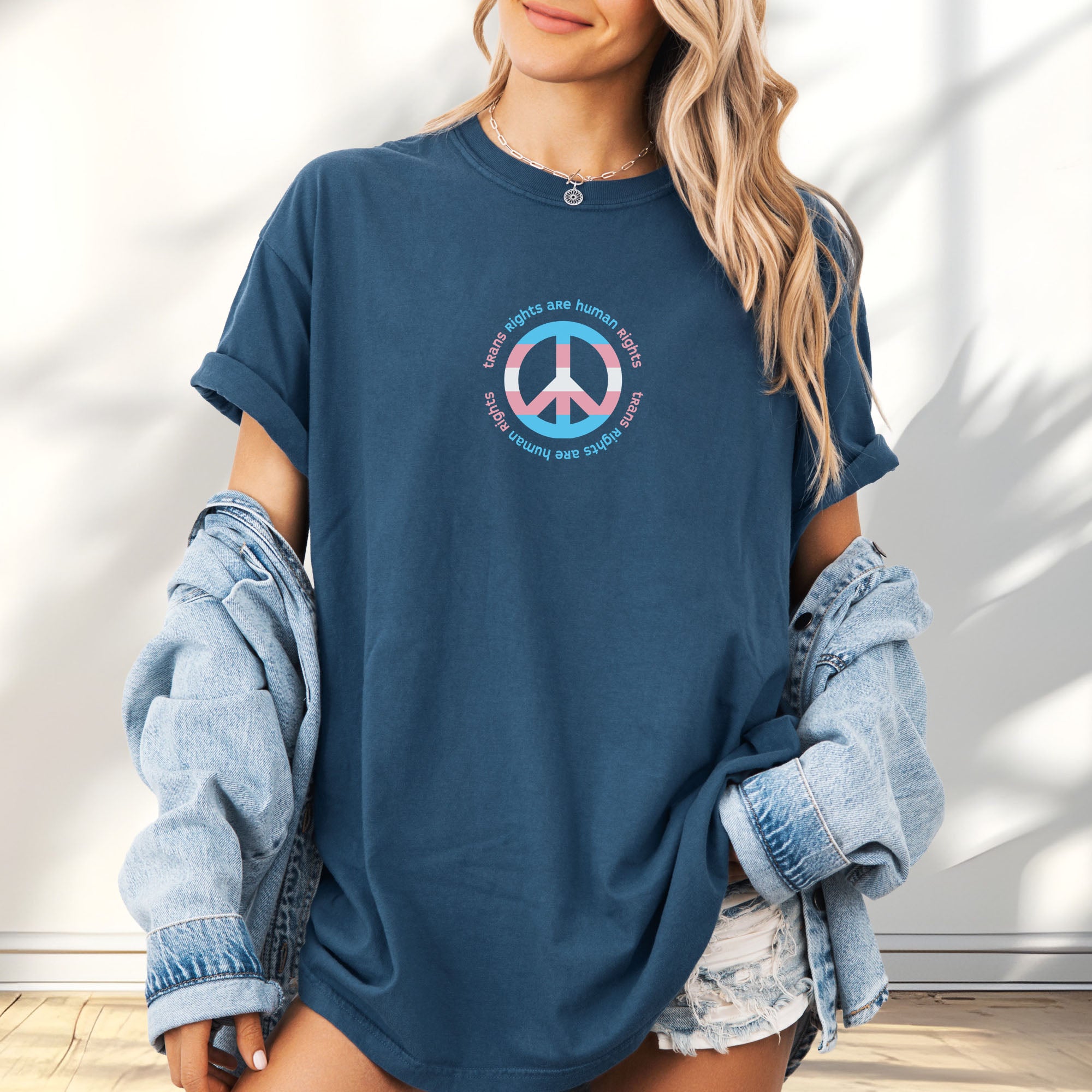 Female model wearing oversized midnight t-shirt with a peace sign in transgender flag colors and the text “Trans Rights Are Human Rights” in a circular design.