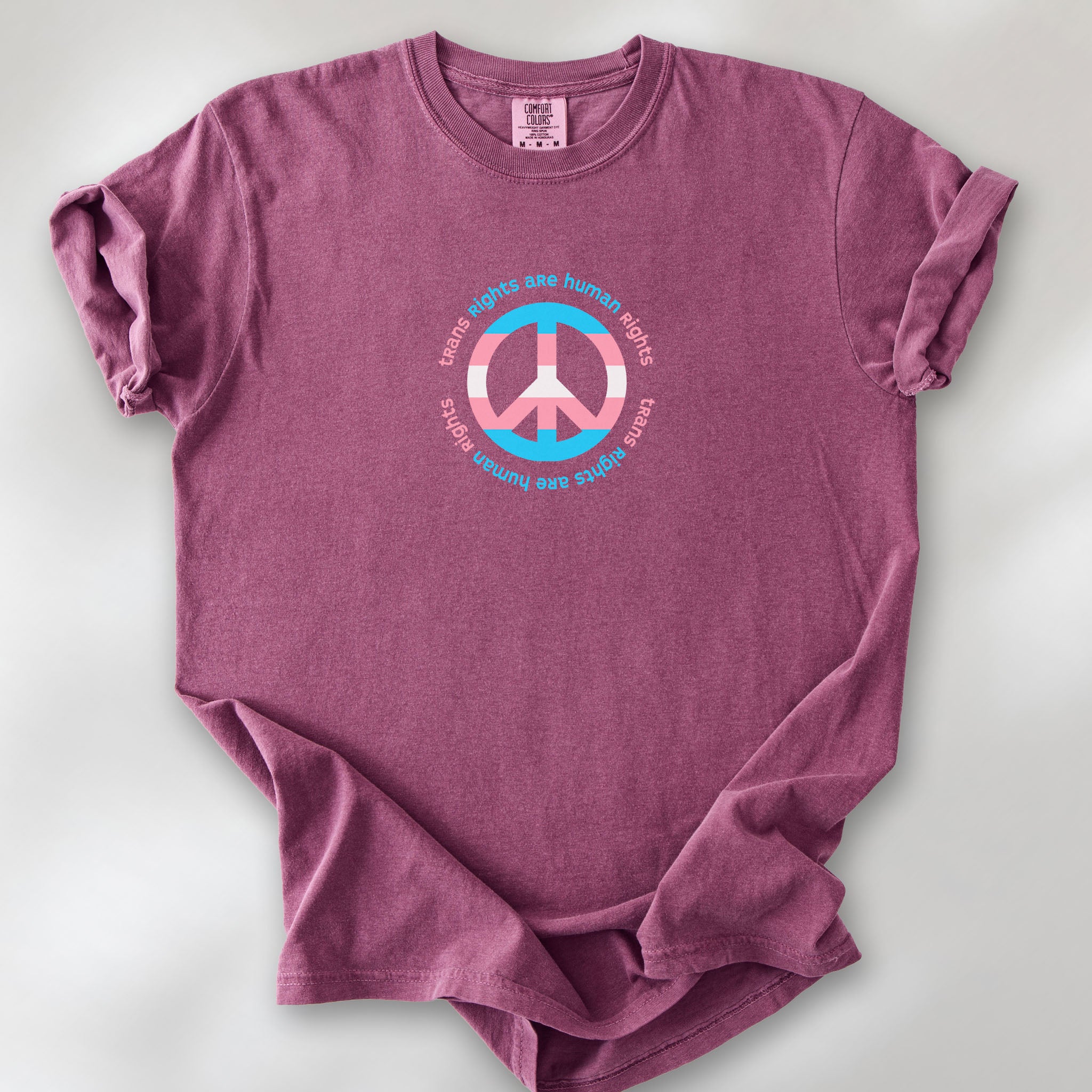 Berry t-shirt with a peace sign in transgender flag colors and the text “Trans Rights Are Human Rights” in a circular design.