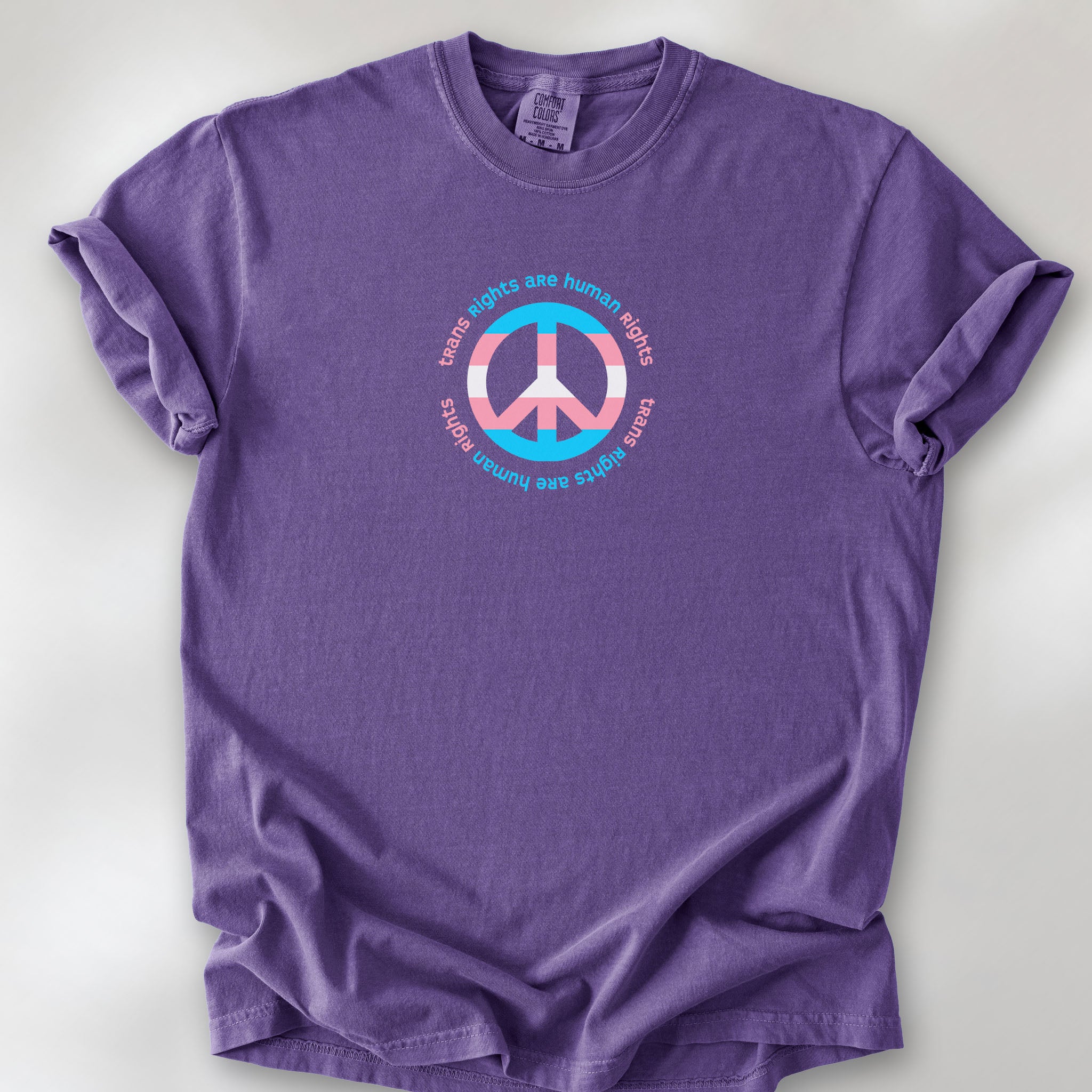Grape t-shirt with a peace sign in transgender flag colors and the text “Trans Rights Are Human Rights” in a circular design.