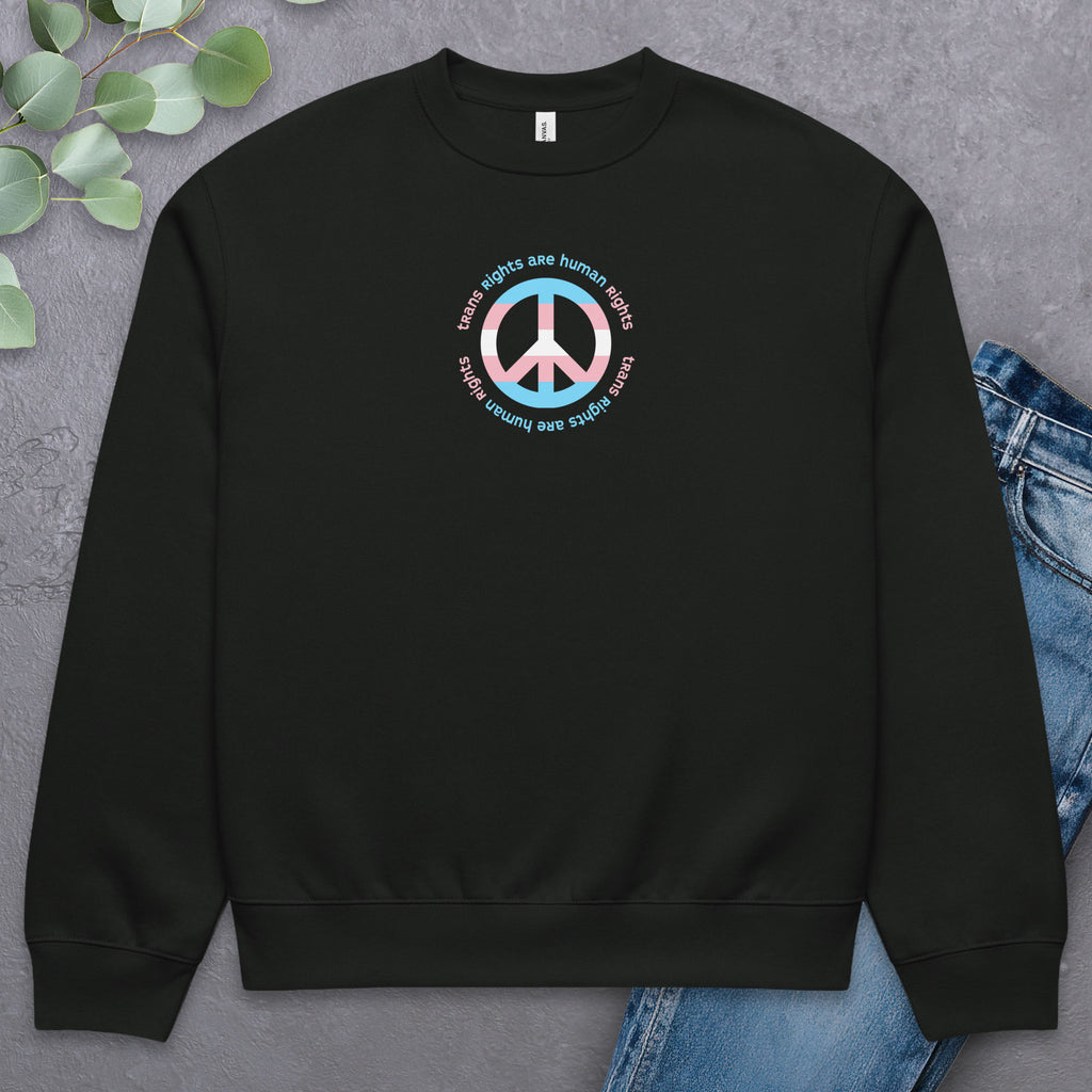Black sweatshirt with a peace sign in transgender flag colors and the text “Trans Rights Are Human Rights” in a circular design around the peace sign. Laying flat with a pair of jeans.