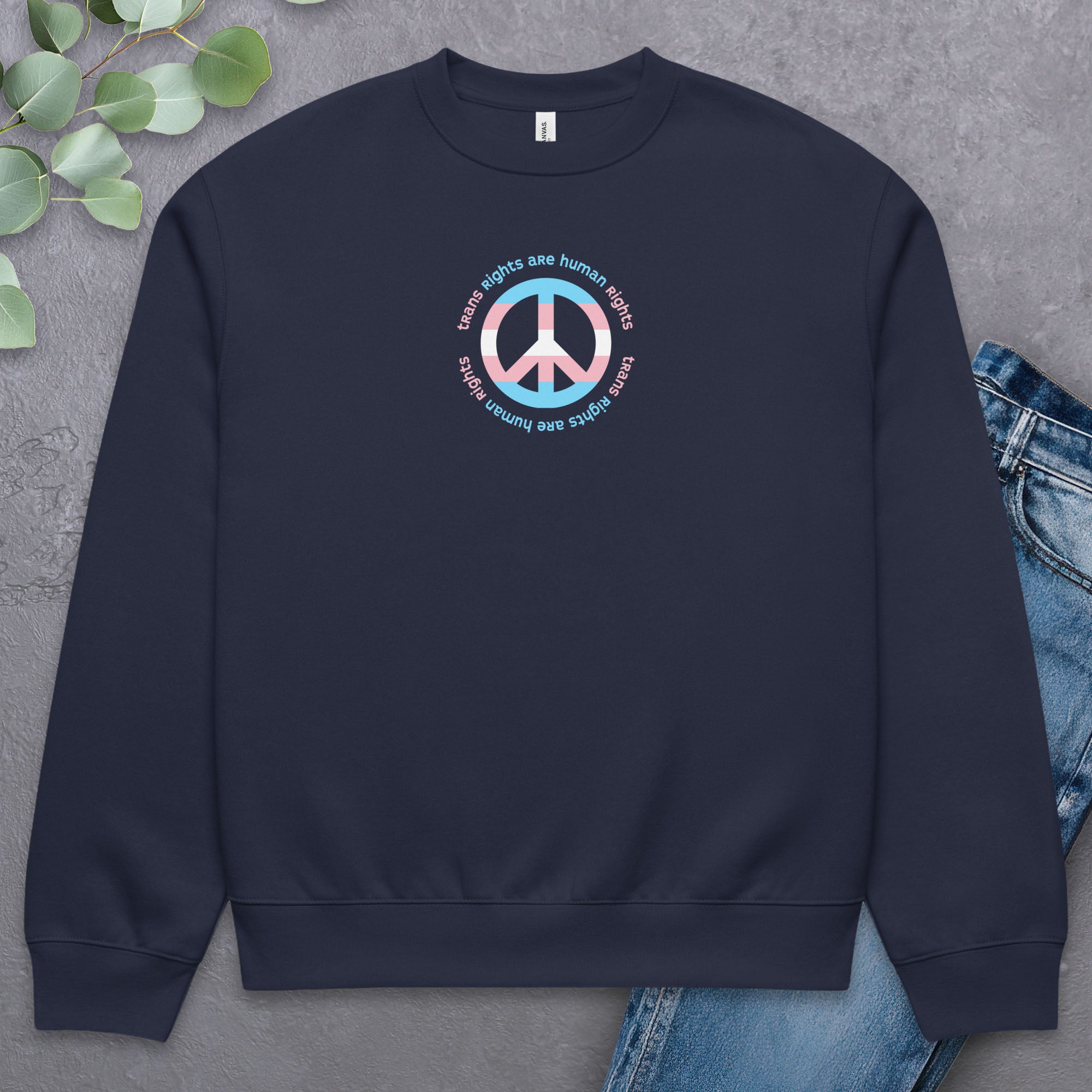 Navy sweatshirt with a peace sign in transgender flag colors and the text “Trans Rights Are Human Rights” in a circular design around the peace sign. Laying flat with a pair of jeans.