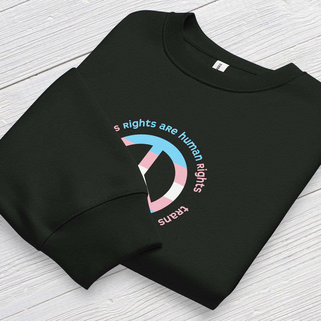 Black sweatshirt with a peace sign in transgender flag colors and the text “Trans Rights Are Human Rights” in a circular design around the peace sign. Folded showing cuff detail.