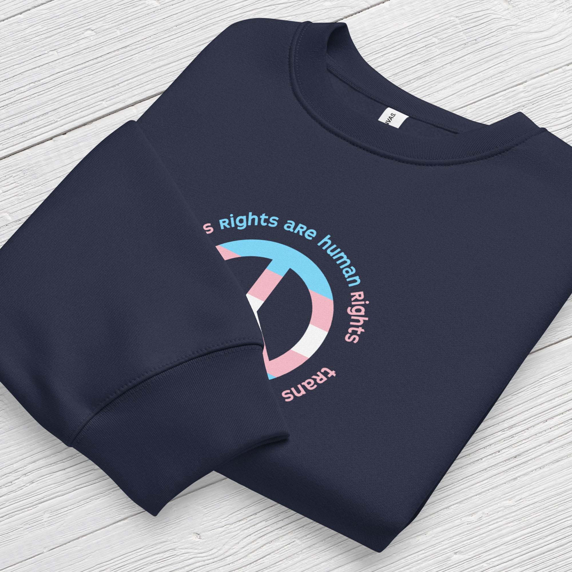 Navy sweatshirt with a peace sign in transgender flag colors and the text “Trans Rights Are Human Rights” in a circular design around the peace sign. Folded showing cuff detail.