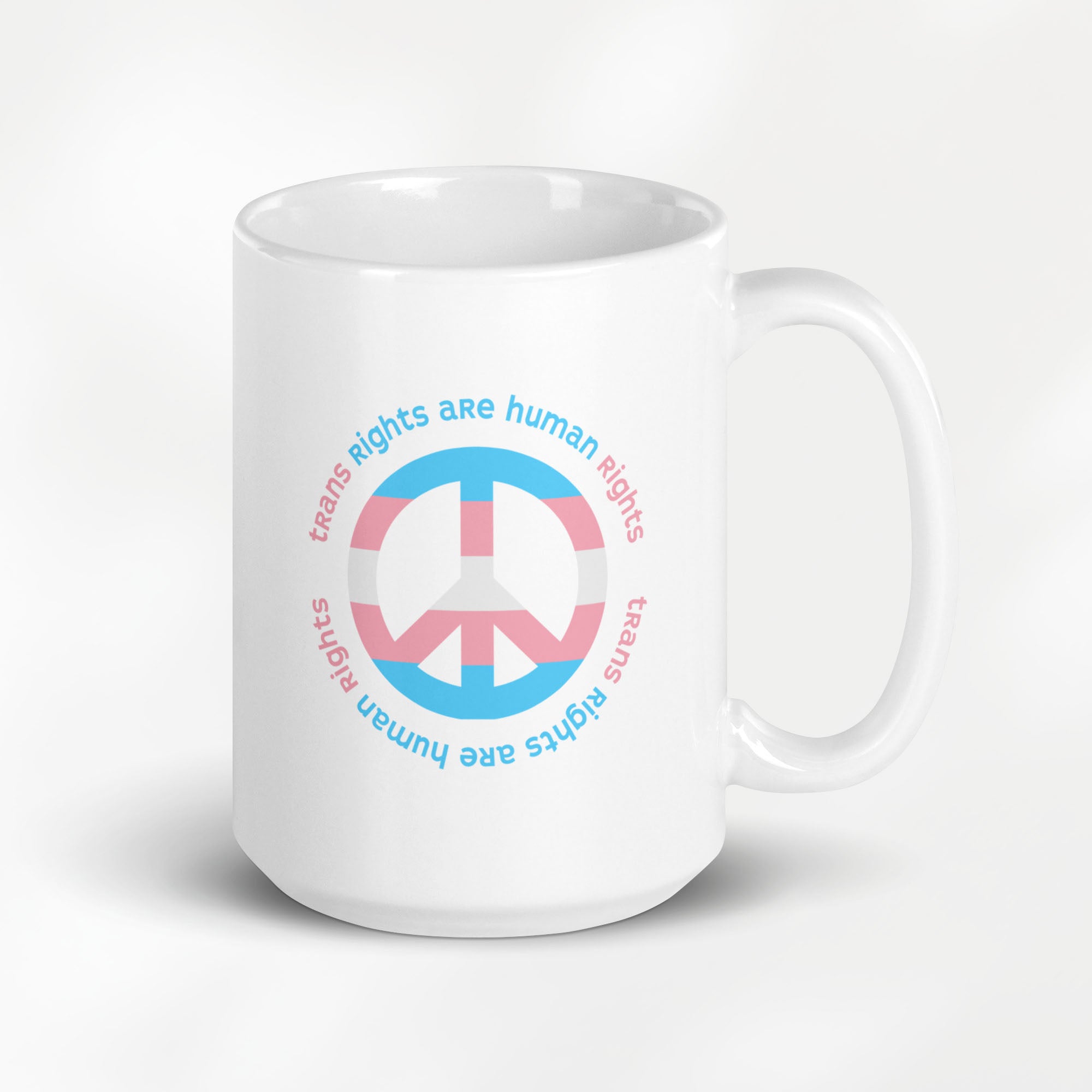 15 ounce ceramic mug with a peace sign in transgender flag colors and the text “Trans Rights Are Human Rights” in a circular design around the peace sign.