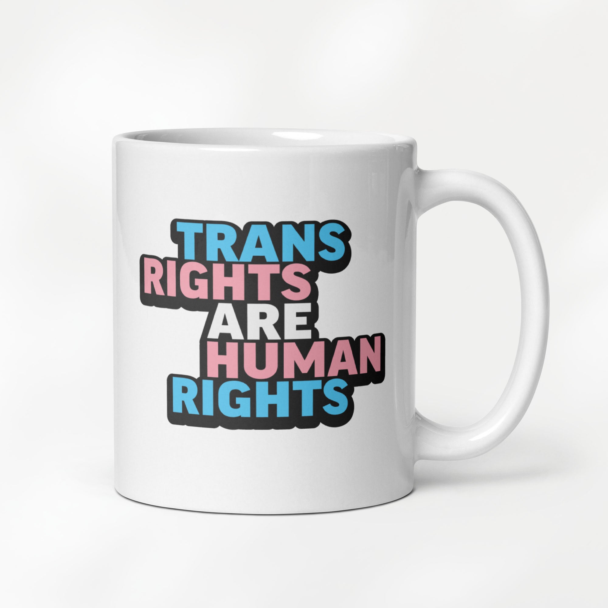 11 ounce white ceramic mug with bold text “Trans Rights Are Human Rights” in blue, pink, and black colors representing the transgender pride flag.