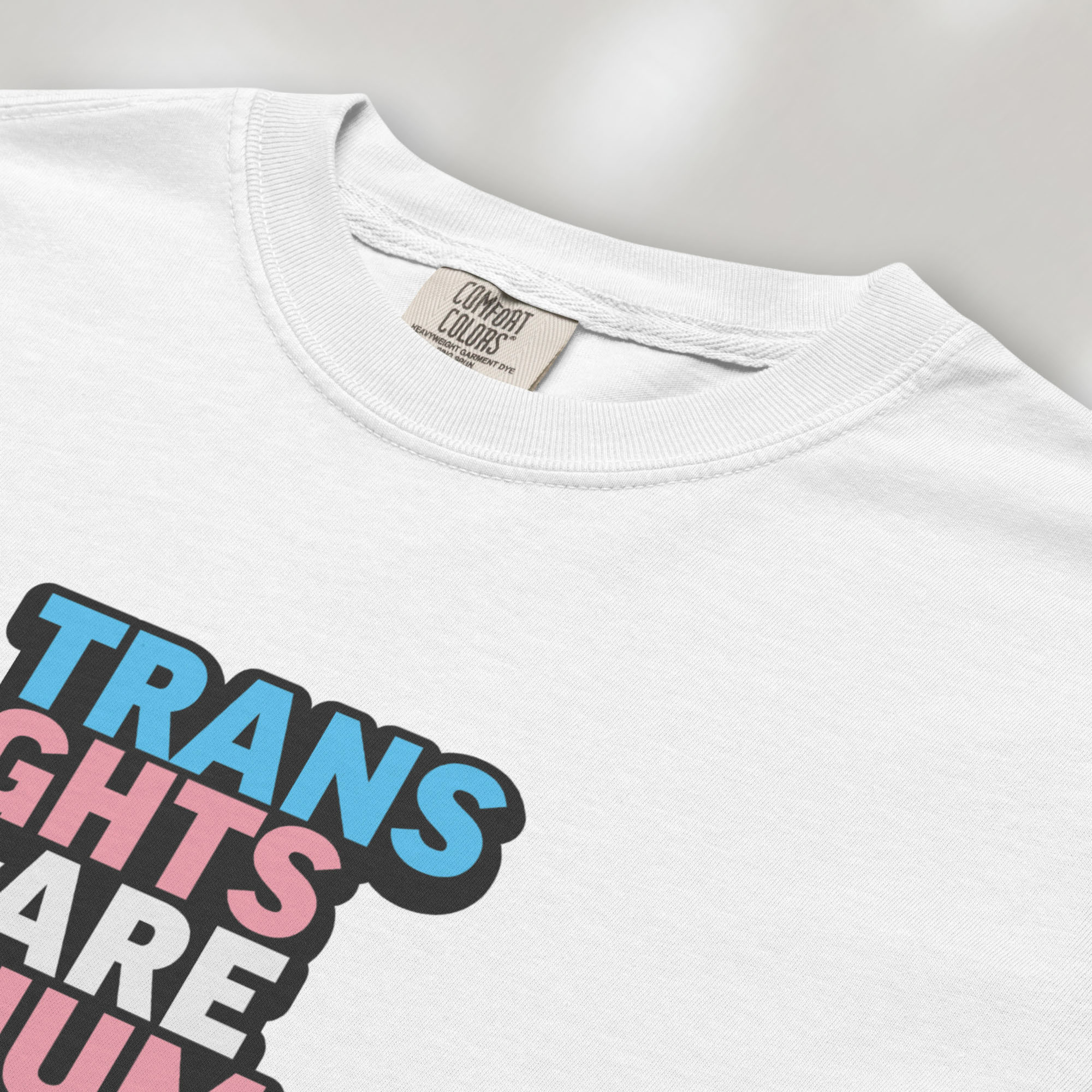 Closeup detail of white t-shirt with graphic reading "trans rights are human rights" in the colors of the trans flag.