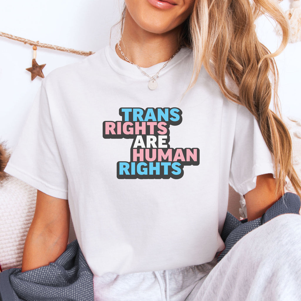Female model wearing white t-shirt with graphic reading "trans rights are human rights" in the colors of the trans flag.