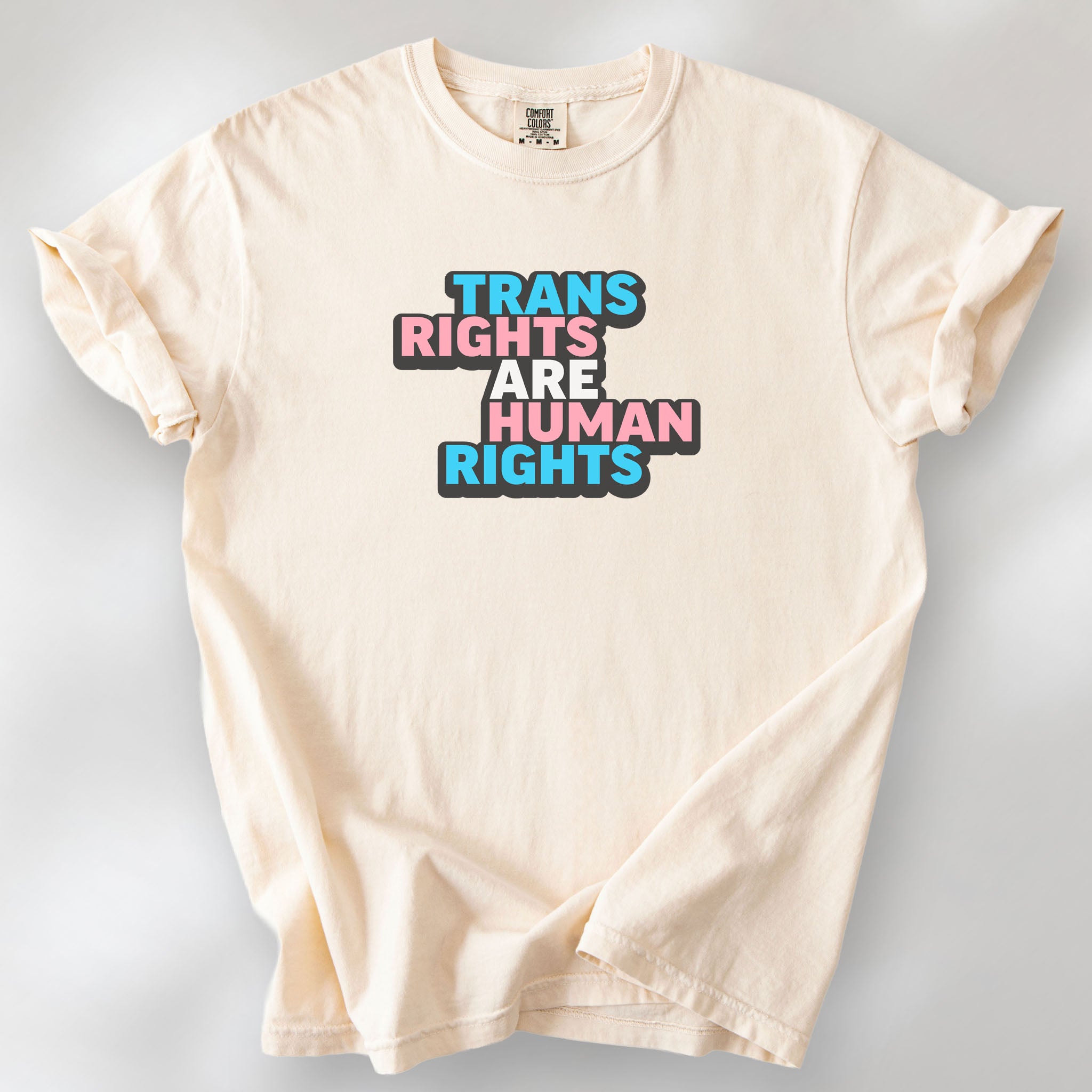 Ivory t-shirt with graphic reading "trans rights are human rights" in the colors of the trans flag.